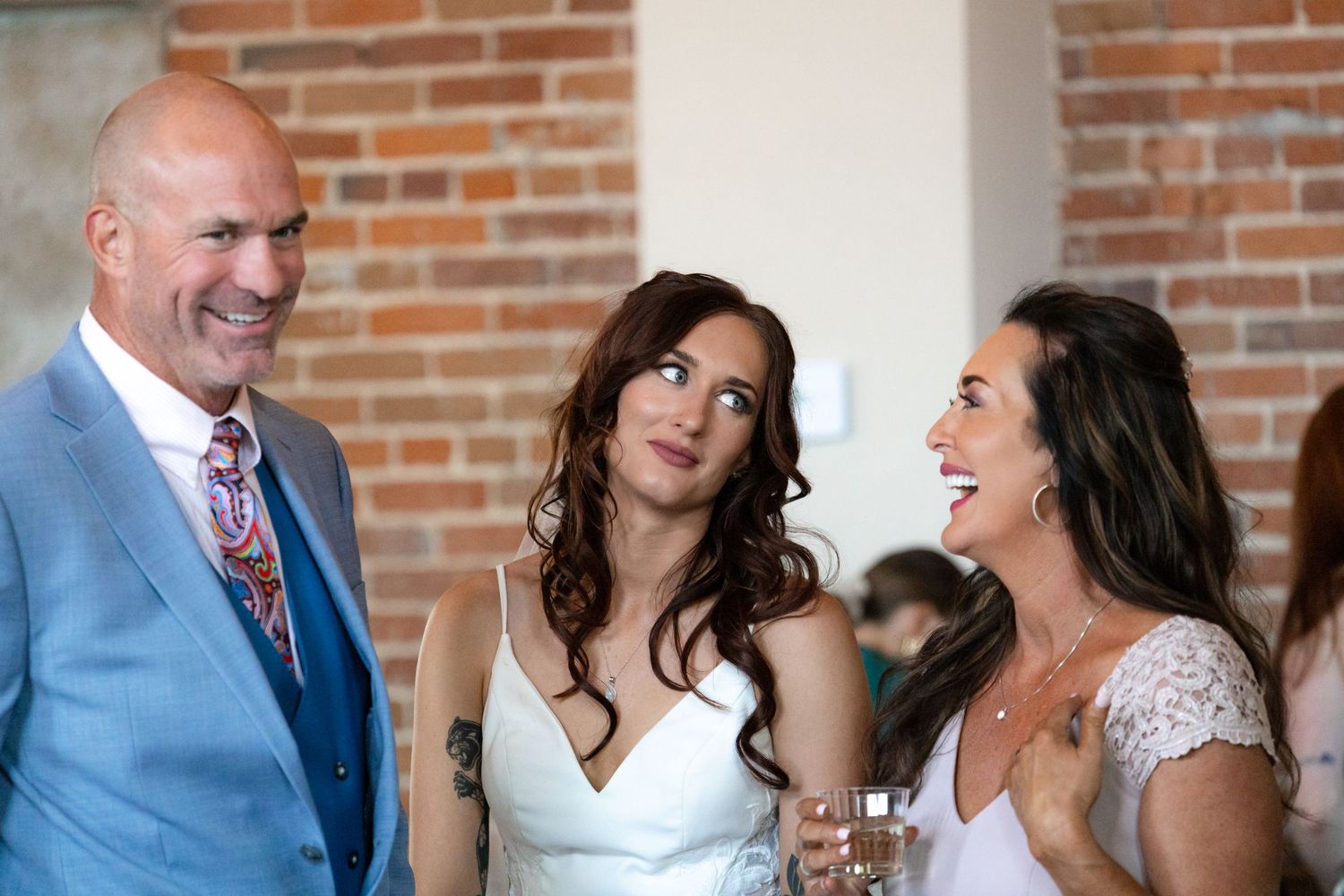 Wedding guests share joyful laughter during reception at rustic brick venue.