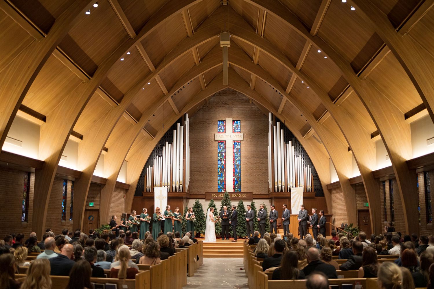 Church interior with vaulted wooden ceiling and rows of pews during wedding ceremony.