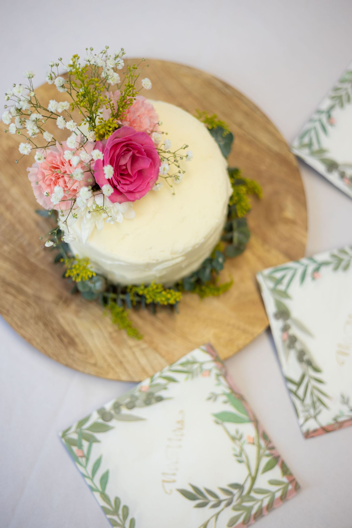 White wedding cake decorated with fresh pink roses and baby's breath on wooden board.