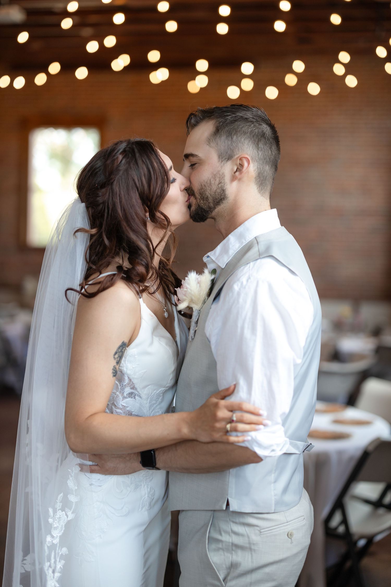 Intimate wedding moment captured in rustic venue with string lights and exposed brick walls.