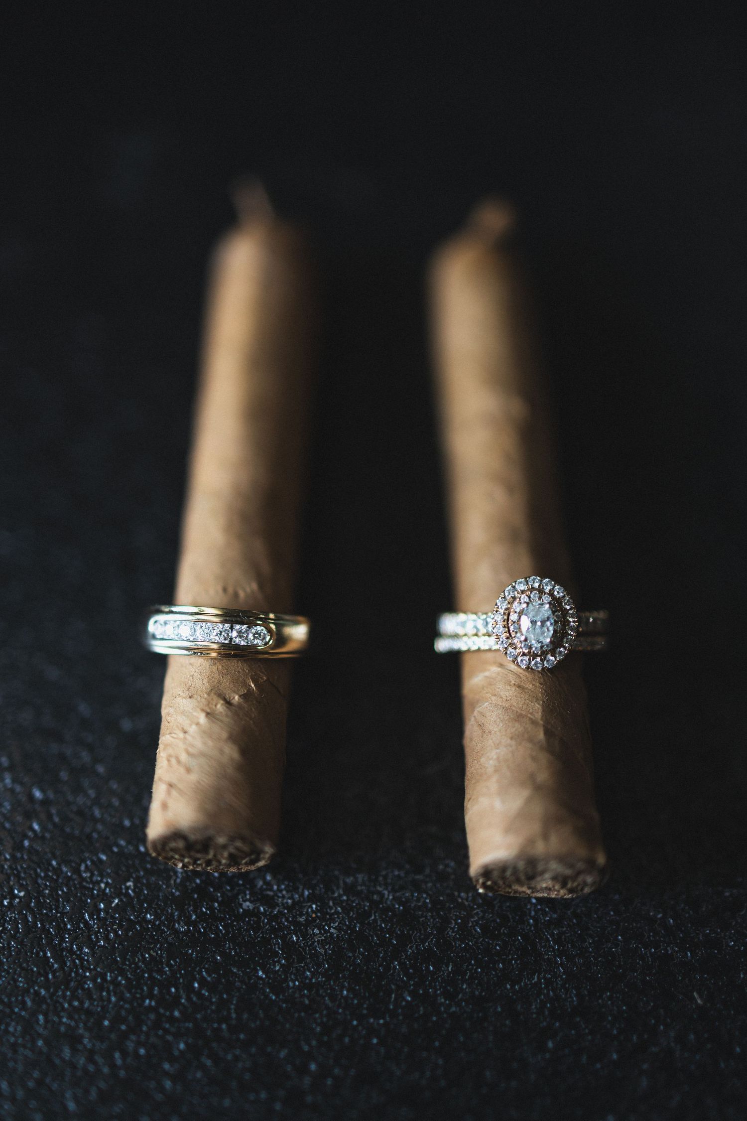Two diamond rings balanced on cigars showing intricate details against black surface.