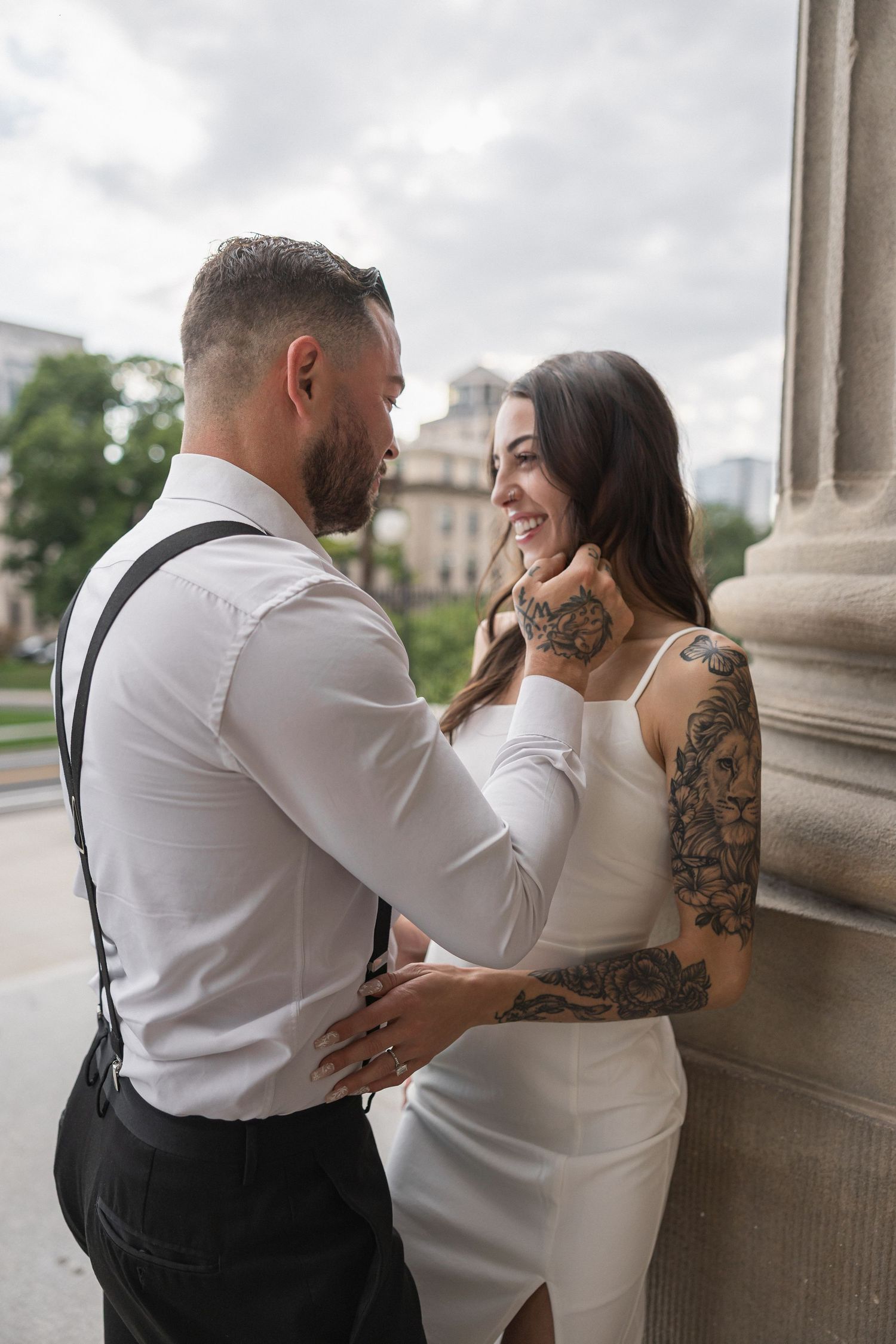 Couple in formal attire share intimate moments against stone columns in a romantic photoshoot series.