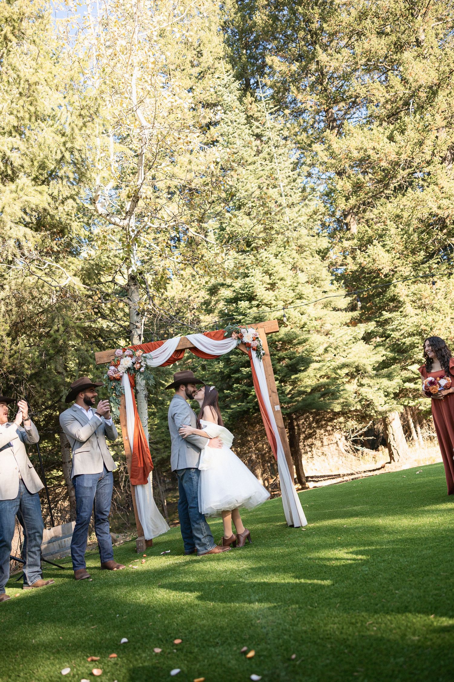 Outdoor wedding ceremony taking place on green lawn surrounded by autumn trees.