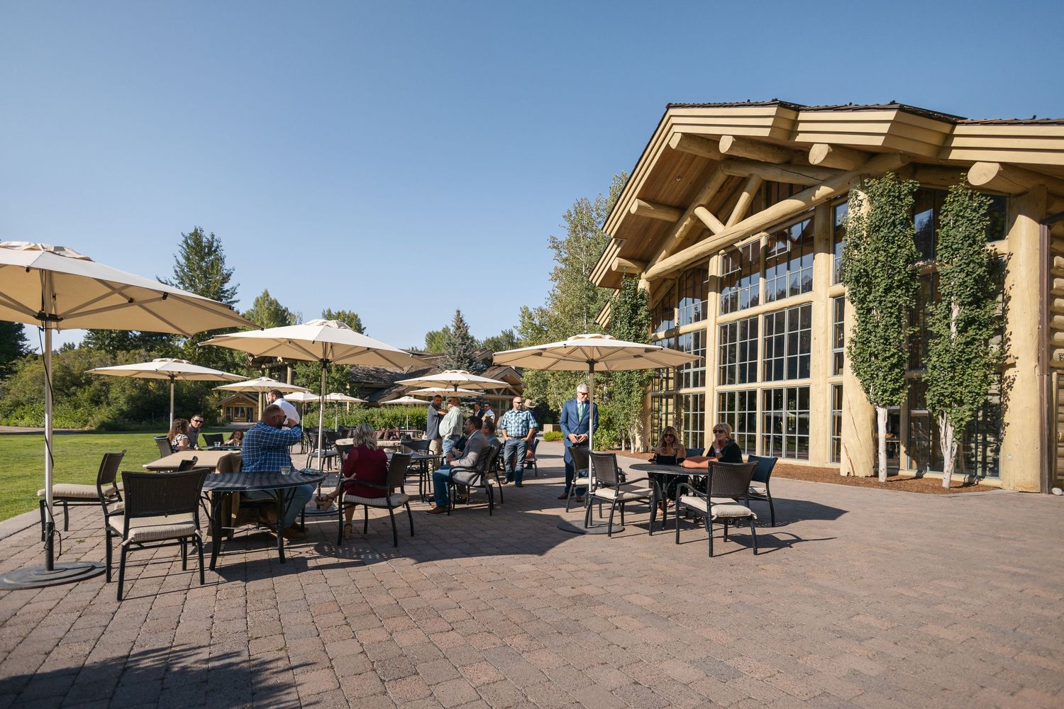 Outdoor patio dining area with umbrellas and tables at an upscale resort building with rustic wooden beams.
