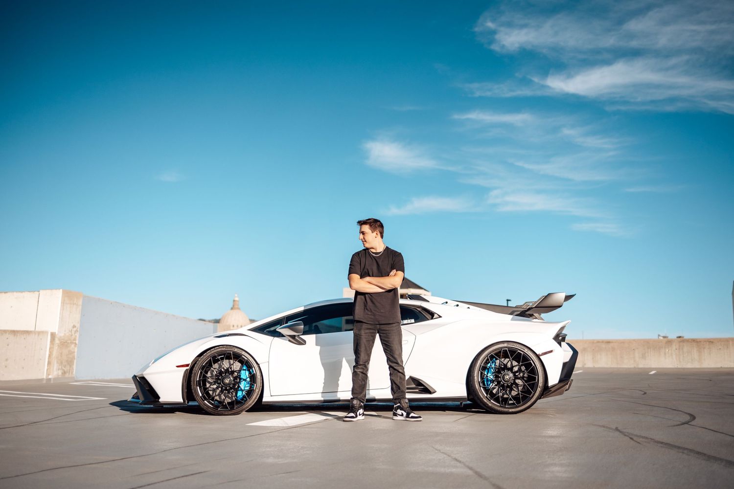 Person in black standing next to white luxury sports car on rooftop parking area.