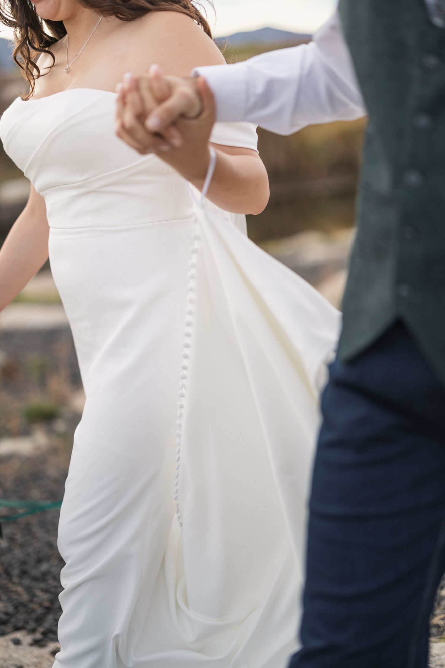 Close-up detail of a wedding dress's intricate button details and flowing fabric.