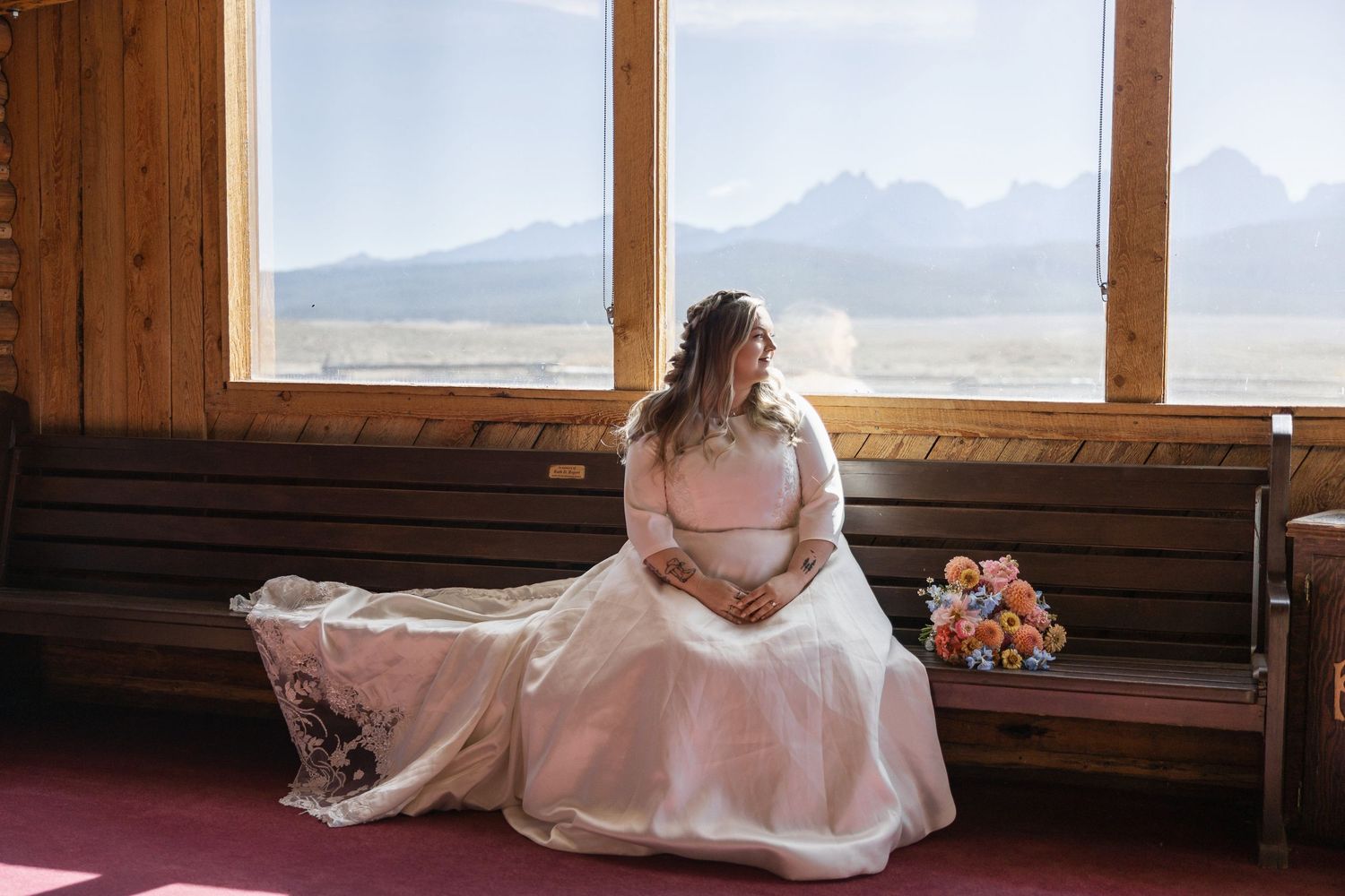 Interior of rustic wooden cabin with large windows showcasing mountain views.