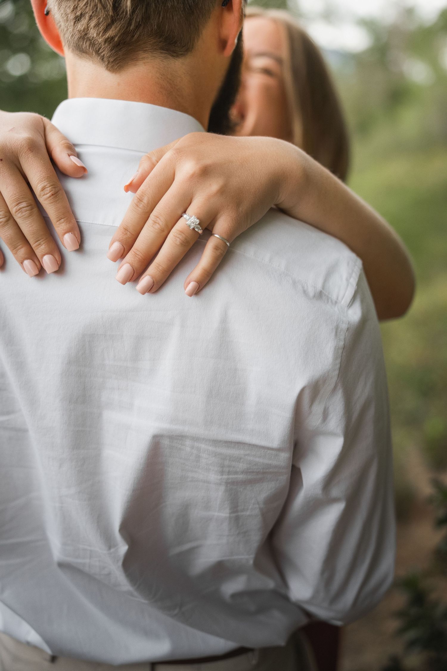 Hands gently embrace a person wearing a white linen shirt, creating an intimate composition against a soft background.