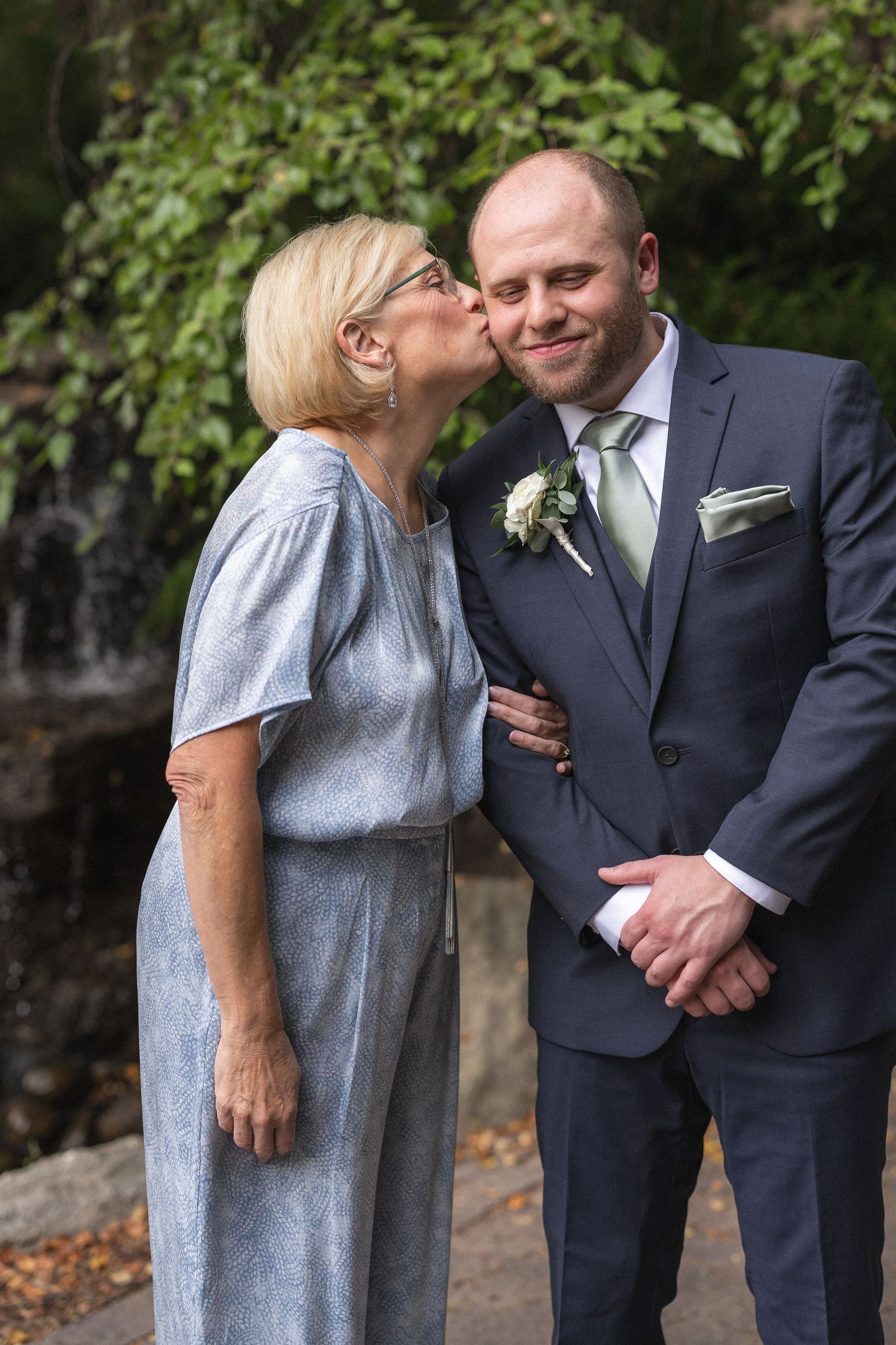 Tender moment captured between wedding guest and groomsman against garden backdrop.