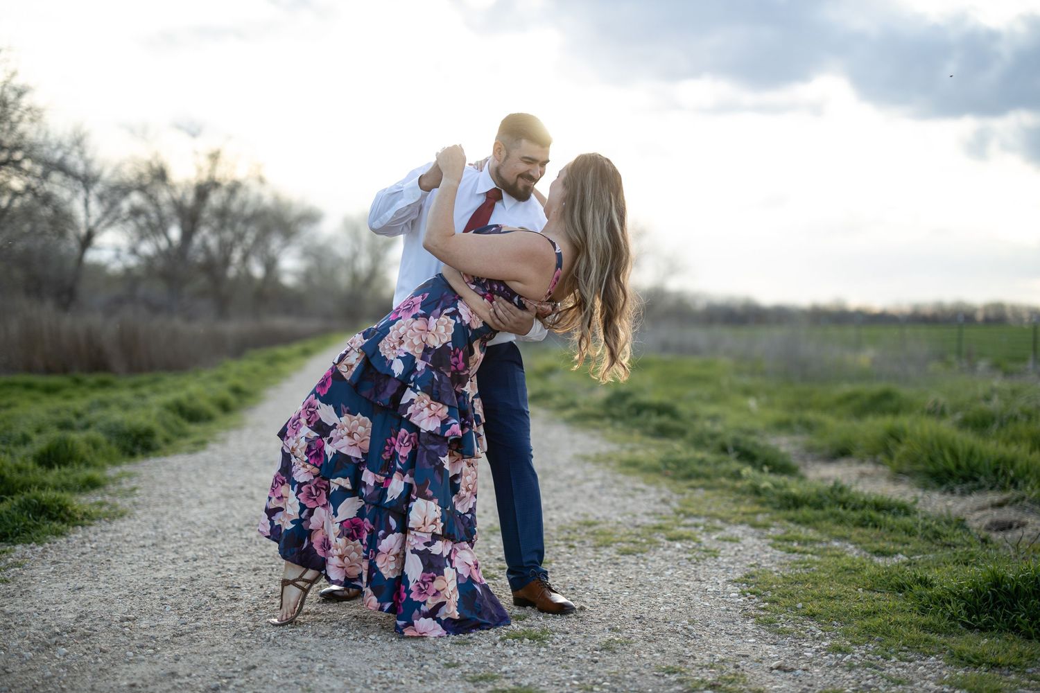 Romantic dance pose on a gravel path with a floral dress twirling against a nature backdrop.