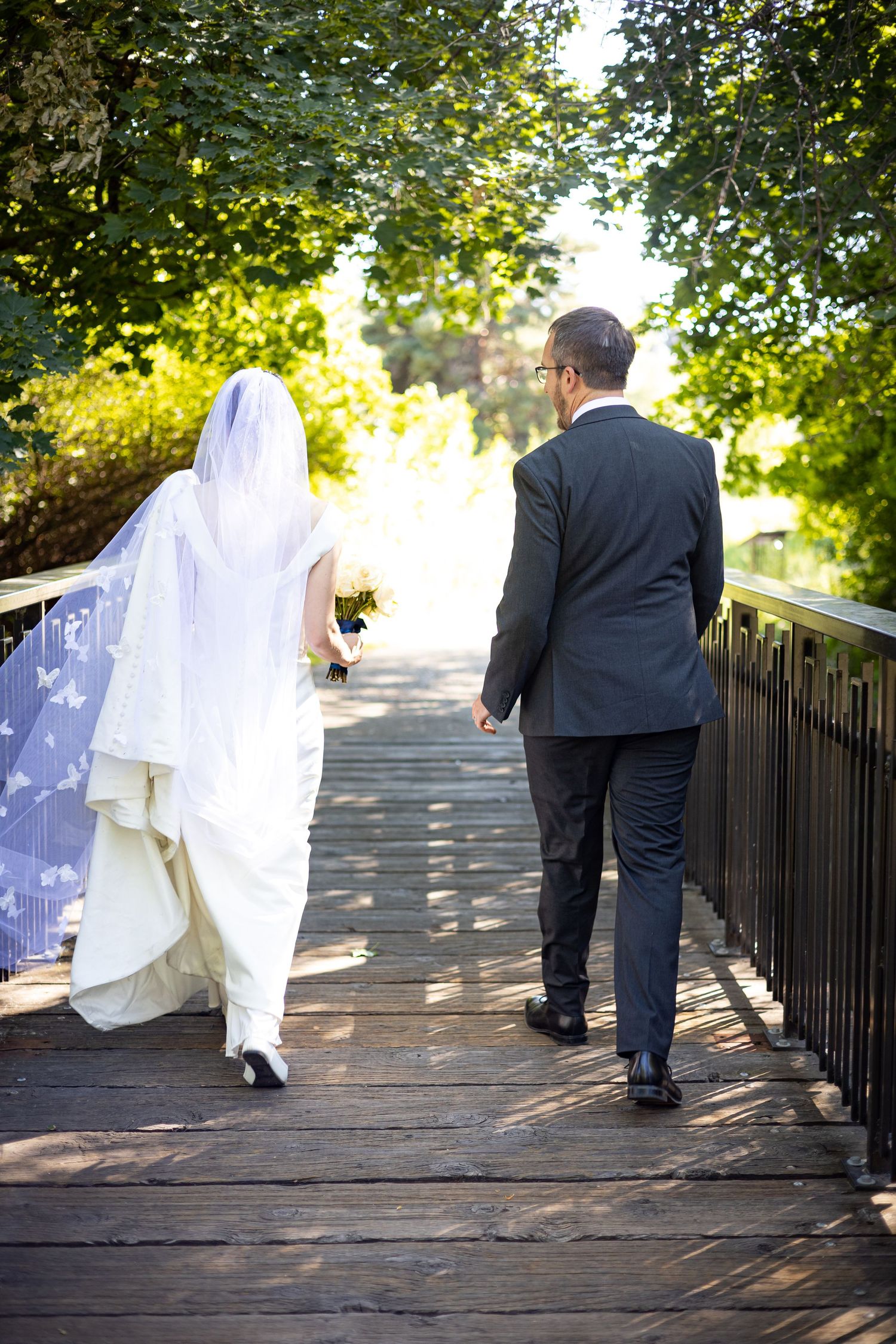 Couple walking away together on a wooden bridge surrounded by trees.