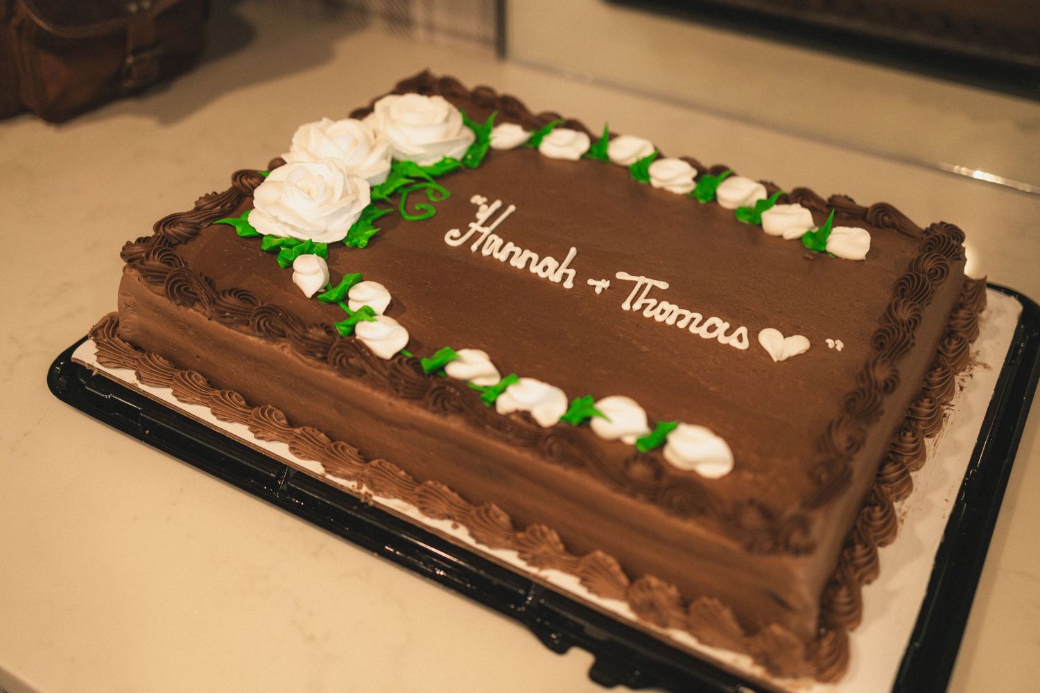 Chocolate wedding cake decorated with white roses and green accents on display.