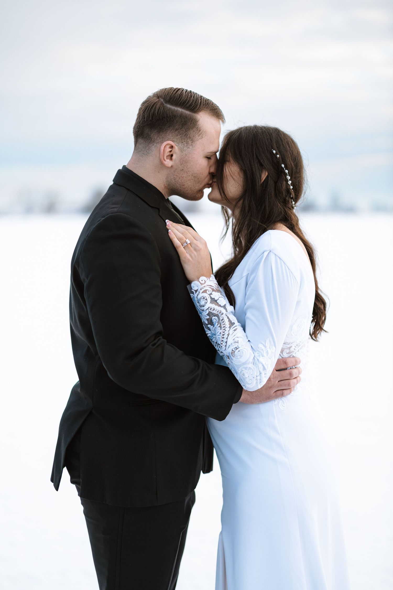 A romantic winter wedding portrait shows a couple in black and white attire embracing in a snowy landscape.