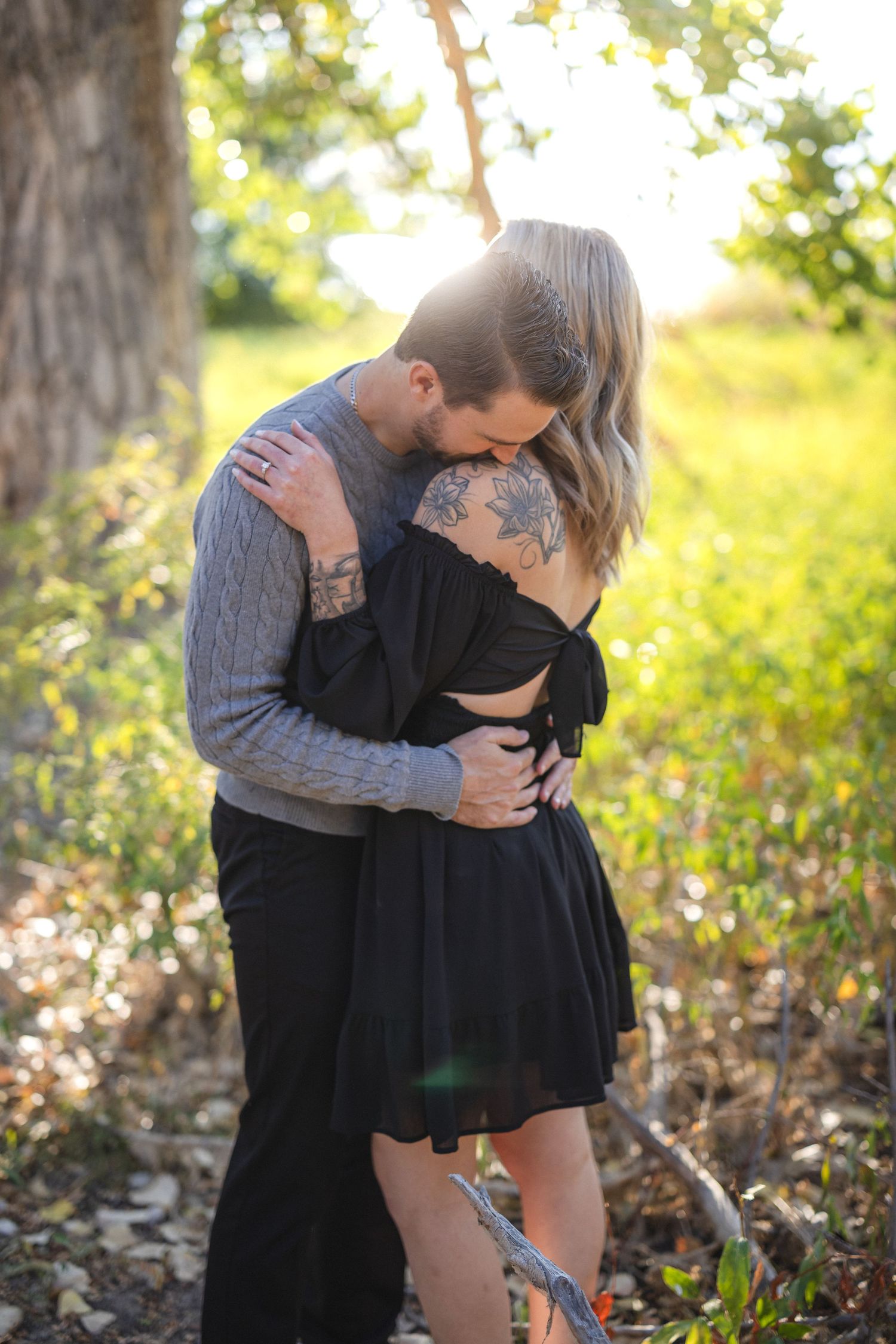 Couple embraces tenderly during outdoor photoshoot with sunlit nature backdrop.