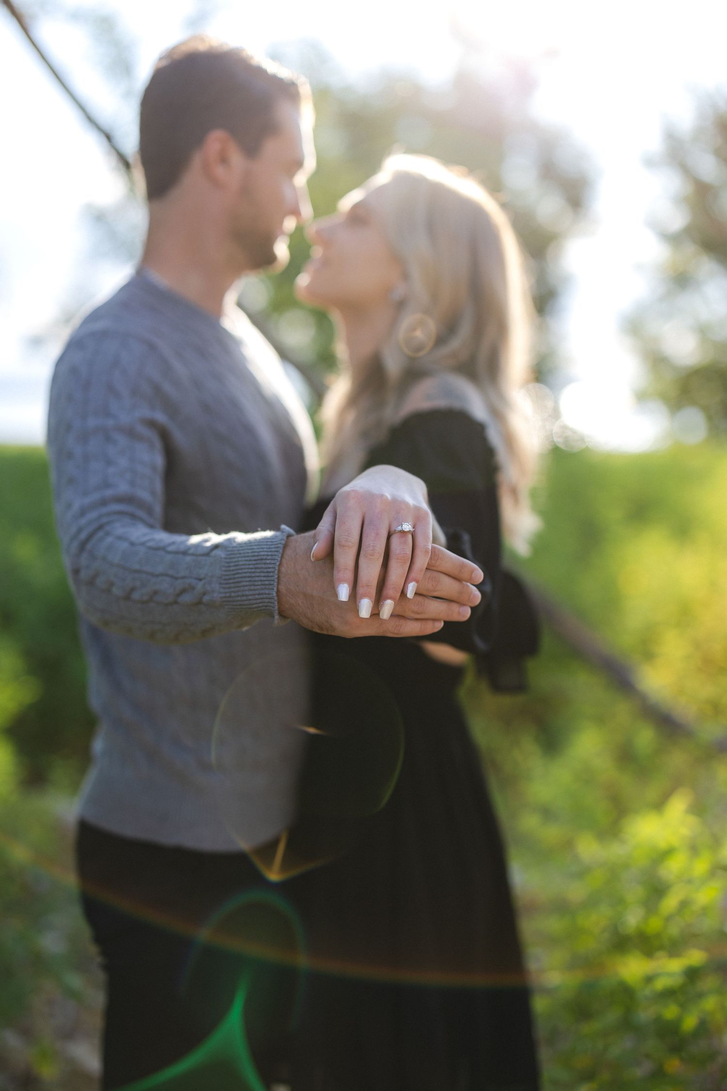 Couple holding hands in outdoor setting with sun flare and natural greenery.