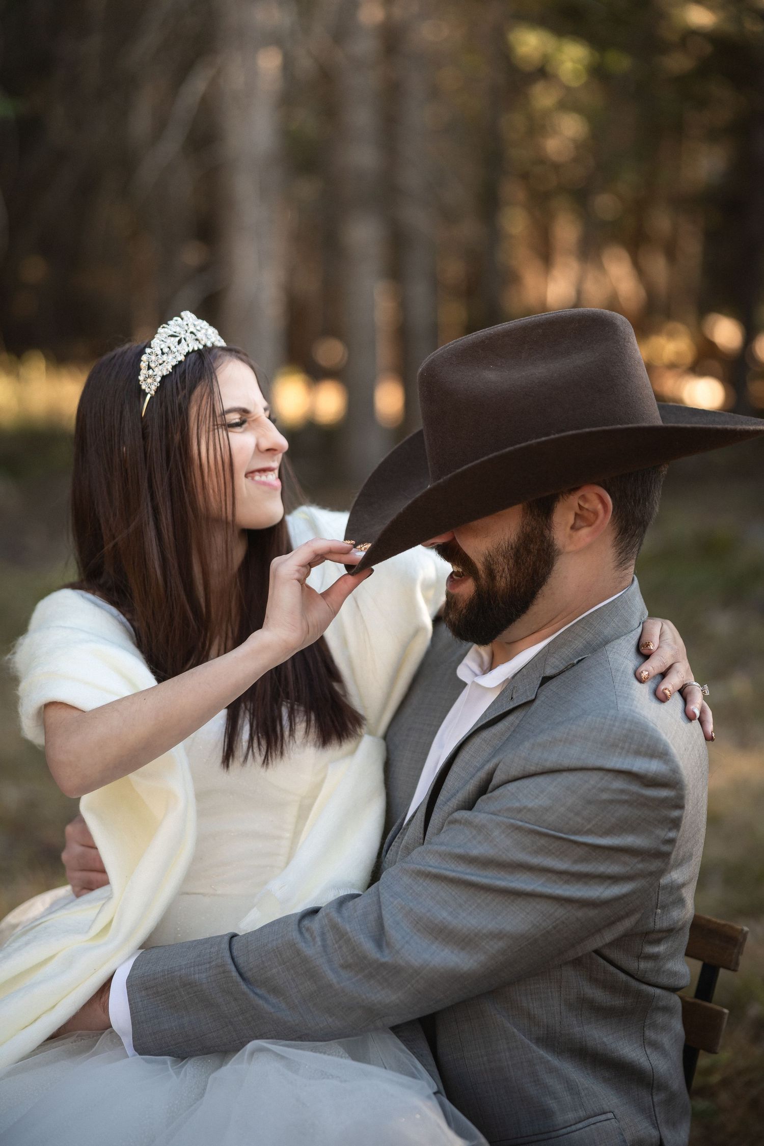 Romantic wedding couple sharing a tender moment with cowboy hat and tiara in forest.
