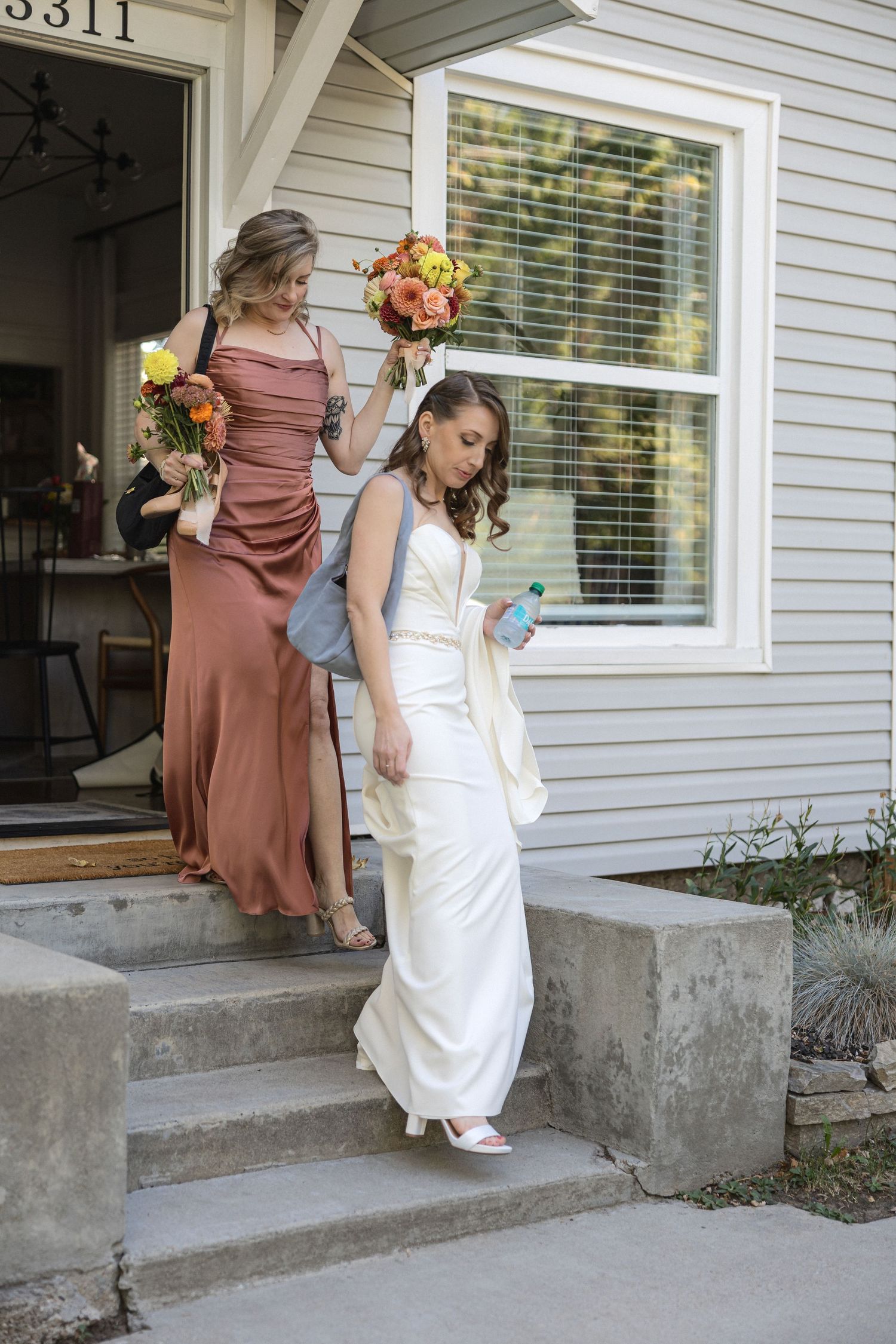 Wedding party descending steps outside house holding floral bouquets.