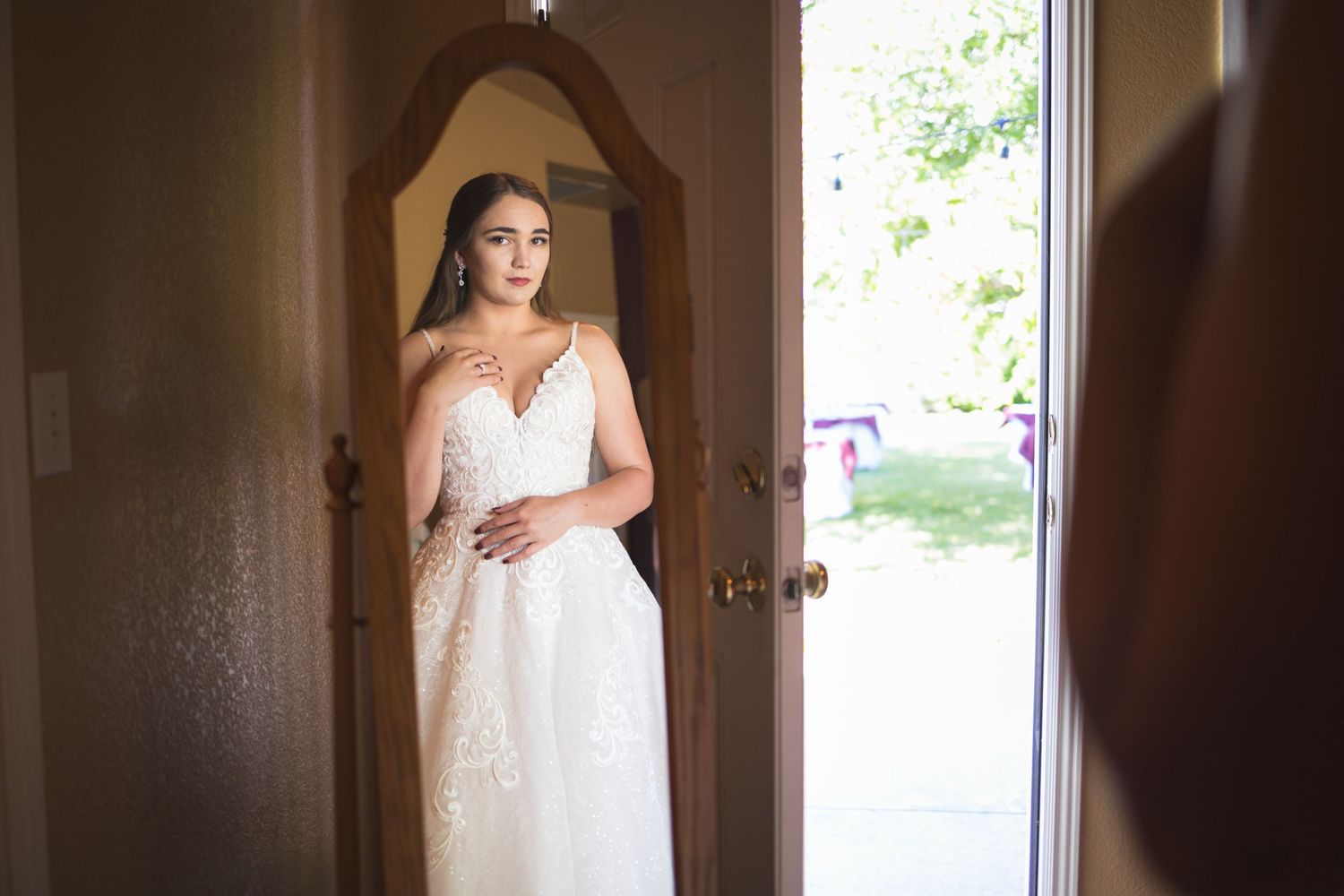 Bride standing in doorway wearing white lace wedding gown with natural lighting.
