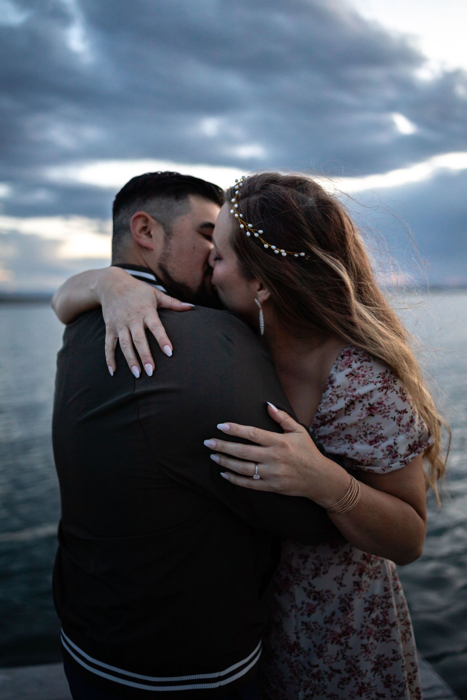 An intimate moment shared between a couple on a dock with moody storm clouds at dusk.