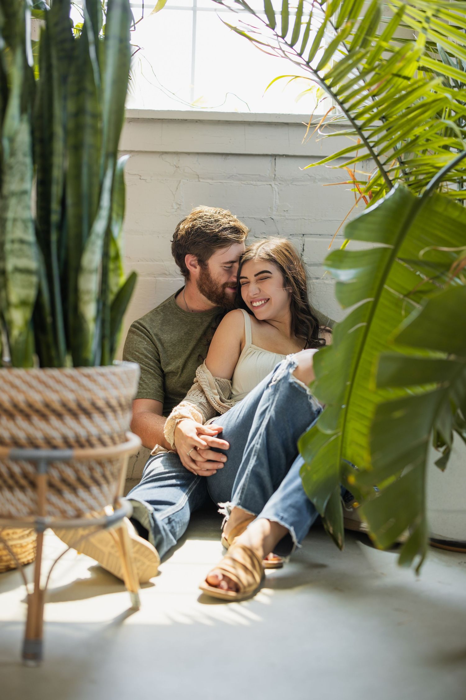 A tender embrace captured between a couple surrounded by lush palm fronds and indoor greenery.
