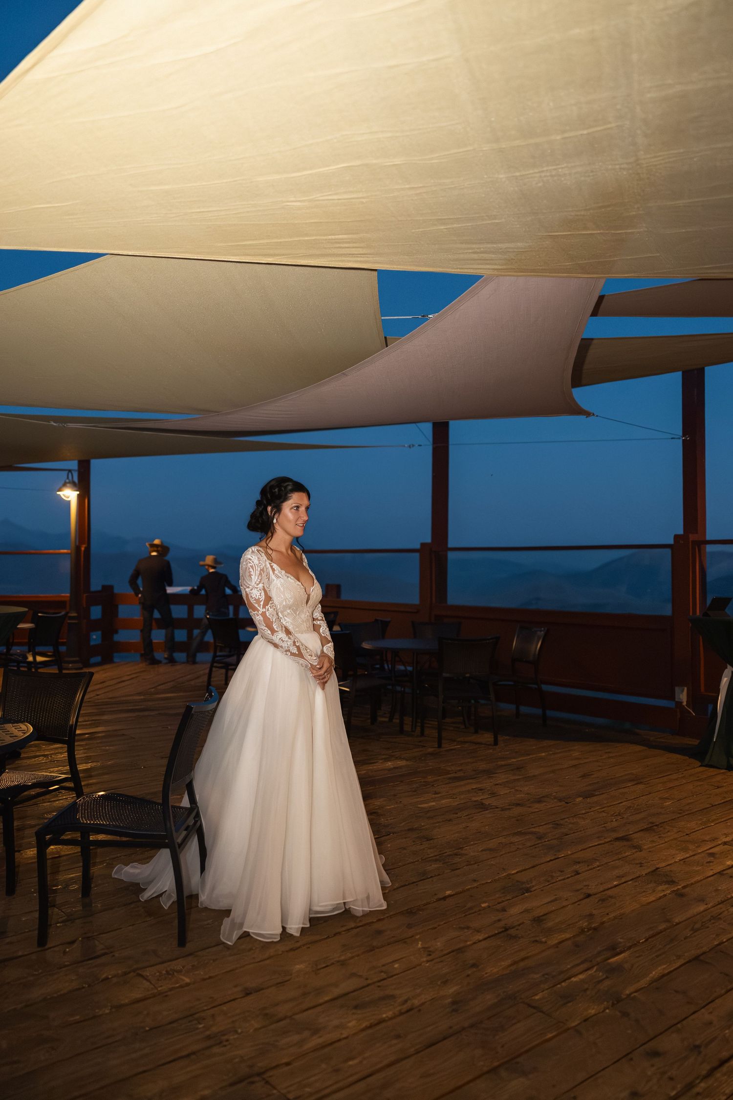 Evening wedding reception venue with white canopy sails and wooden deck overlooking mountains.