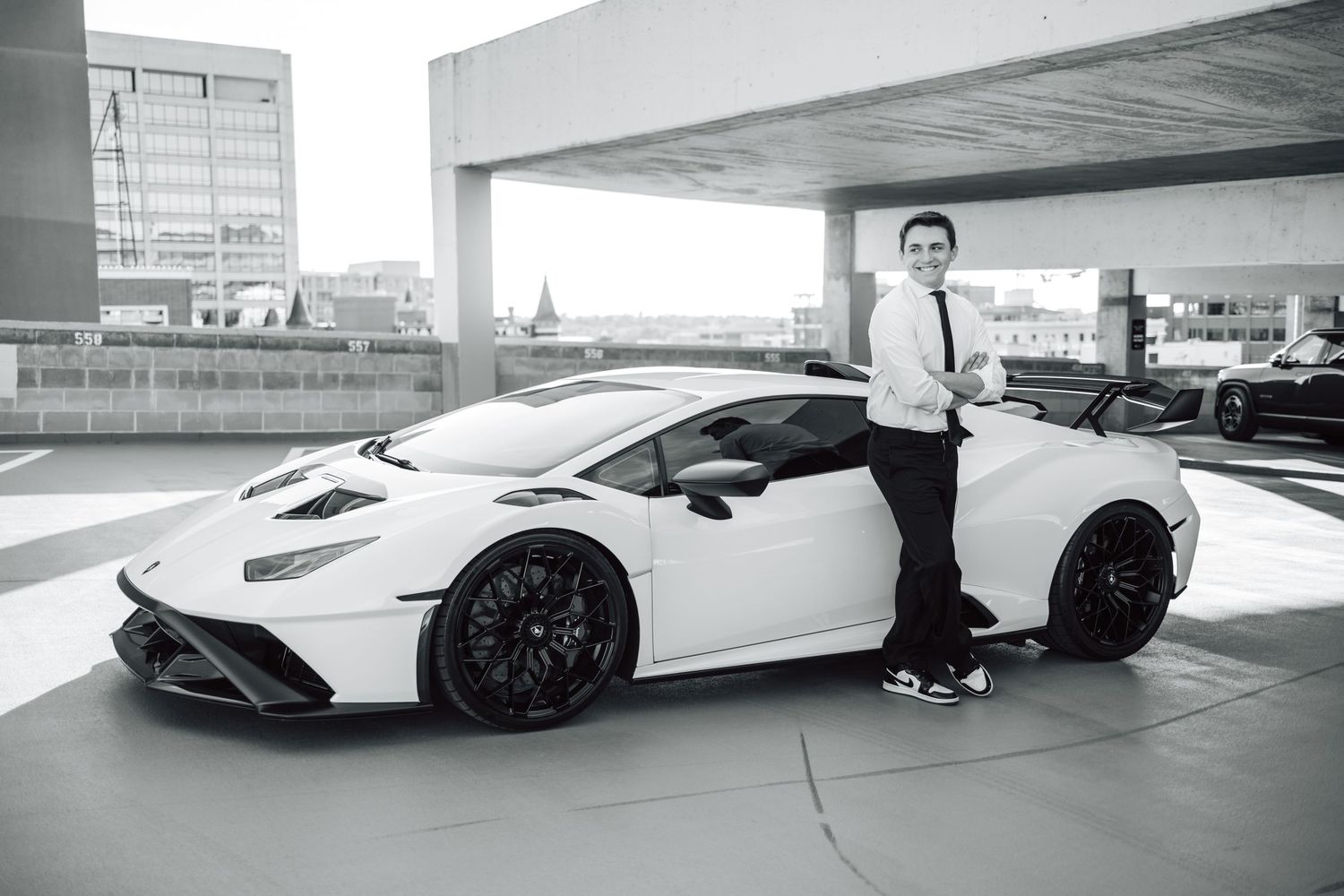 A white Lamborghini Aventador sports car parked in a modern parking structure with someone standing beside it.