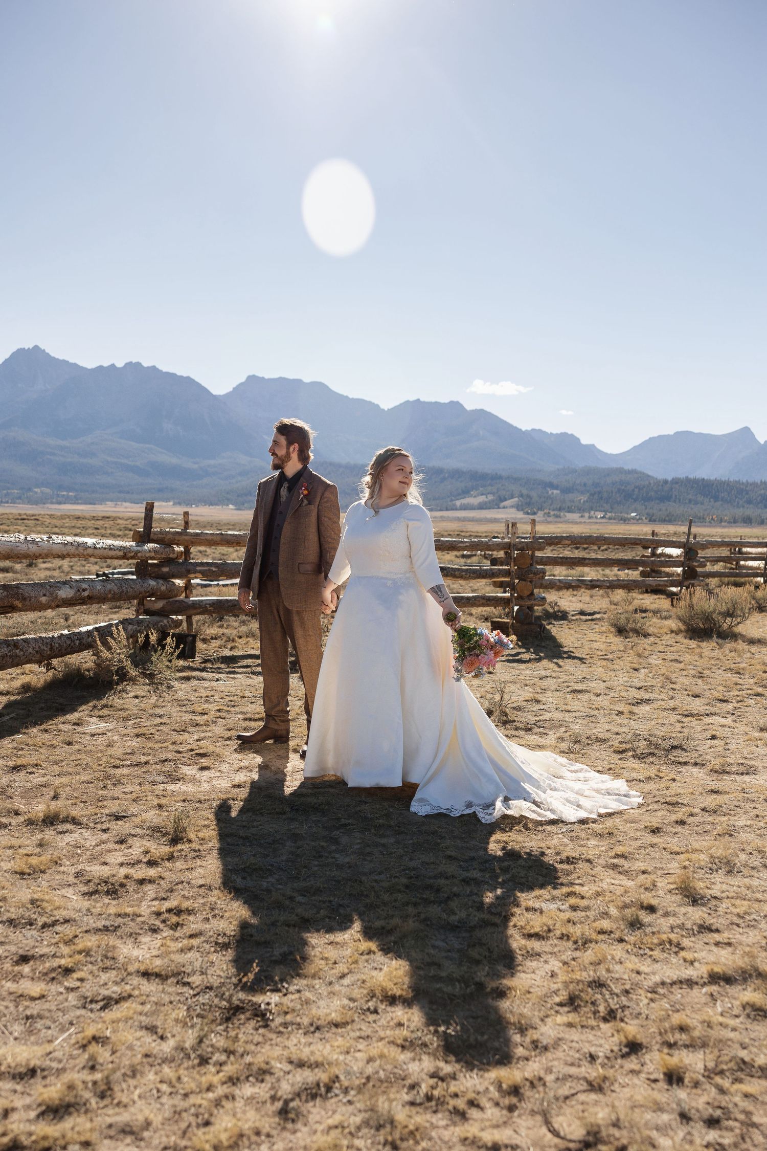 A wedding couple stands silhouetted against a desert landscape with mountains in the background during golden hour.