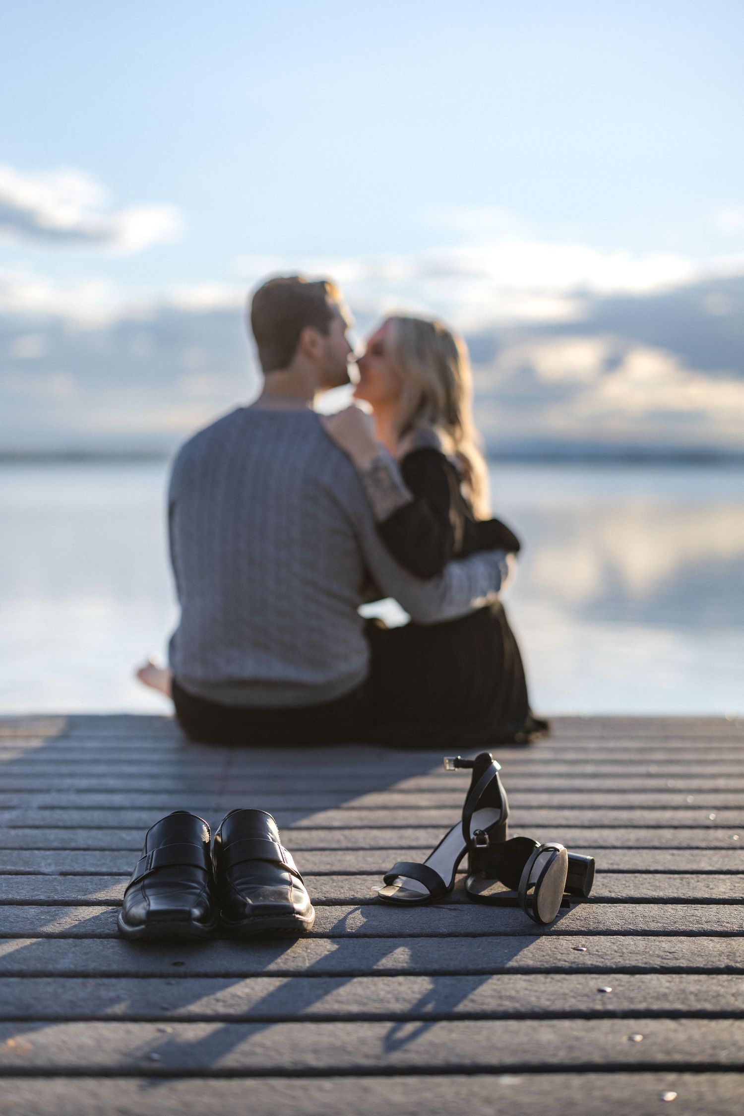 Couple's silhouette on dock with shoes off during intimate sunset moment.