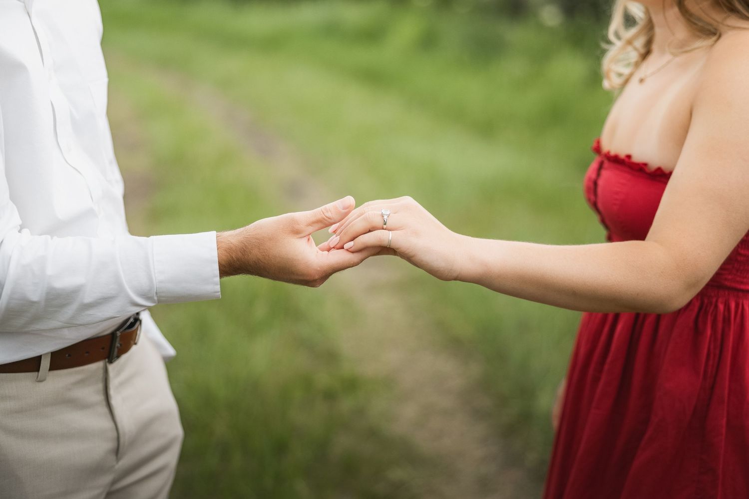 A person in a red dress and someone in a white shirt hold hands in a romantic outdoor garden setting.