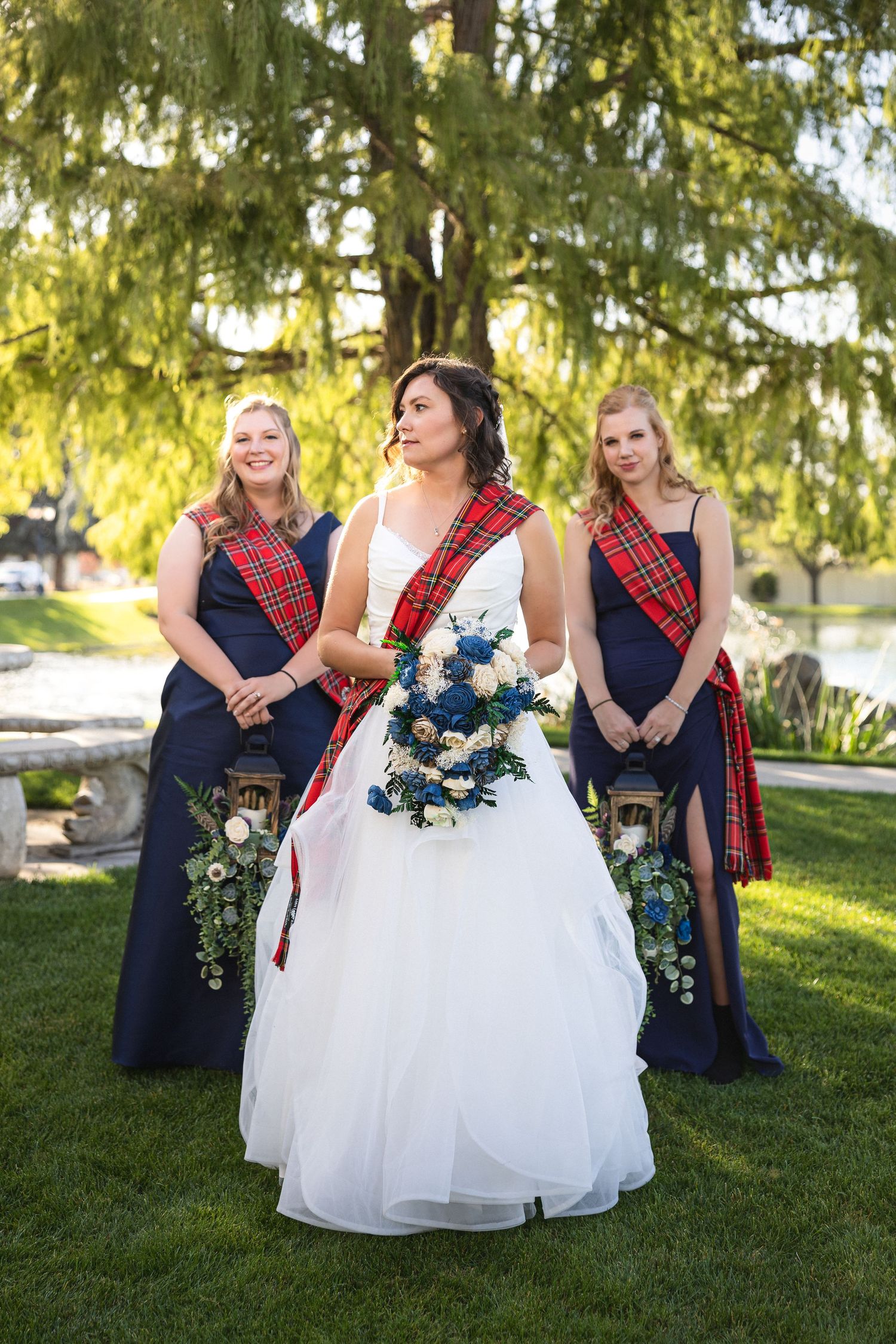 Bride in white gown with red tartan sash poses with bridesmaids in navy dresses and matching sashes.