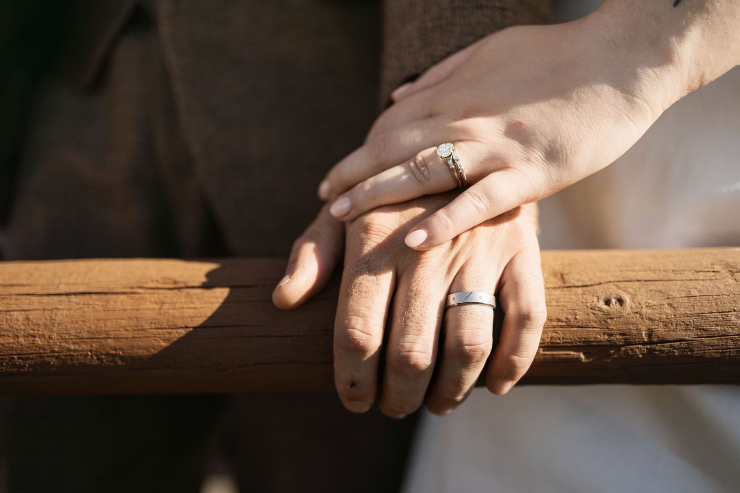 Close-up of hands with wedding rings resting on weathered wooden surface.