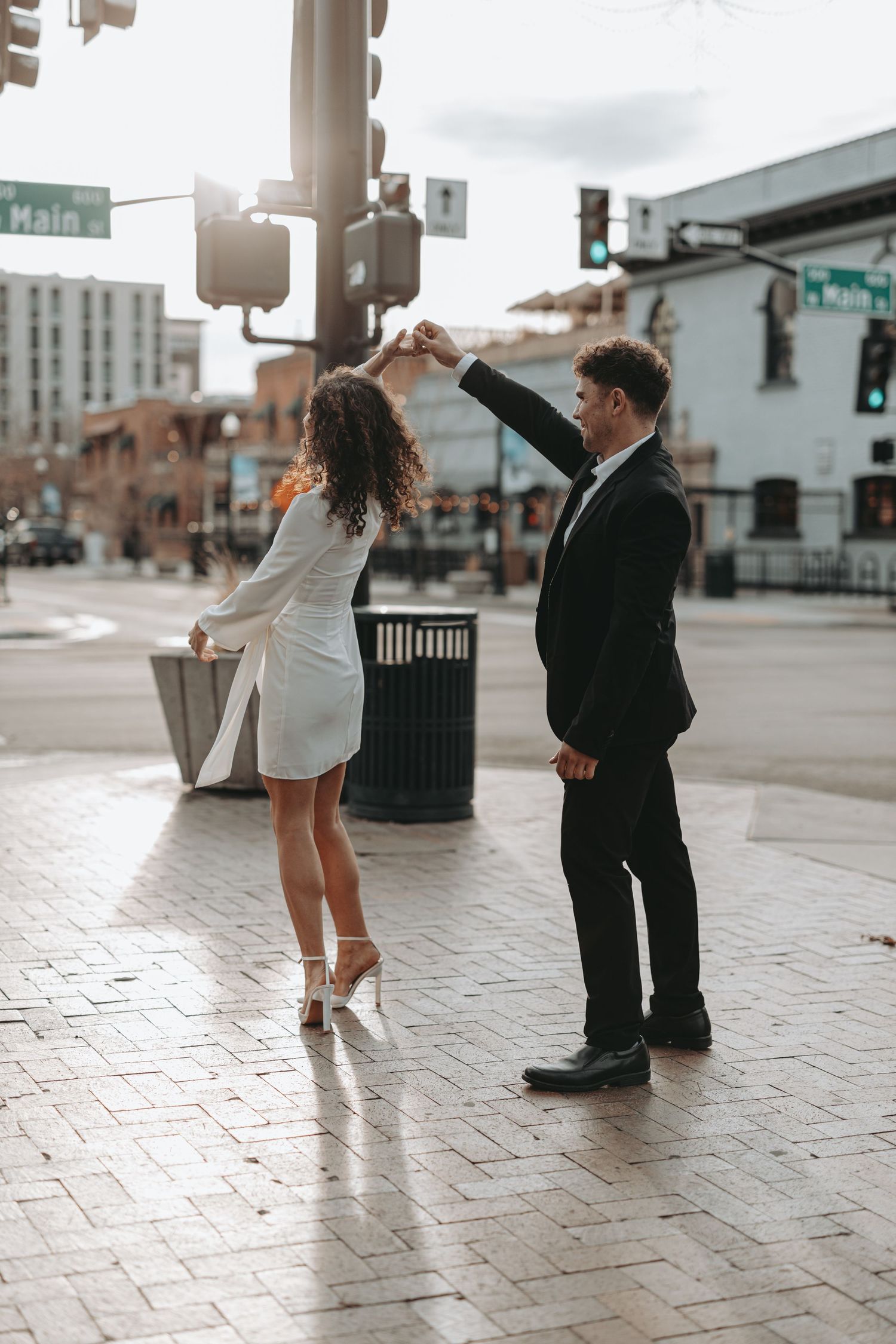 A couple dancing playfully on a downtown street corner with traffic lights overhead.