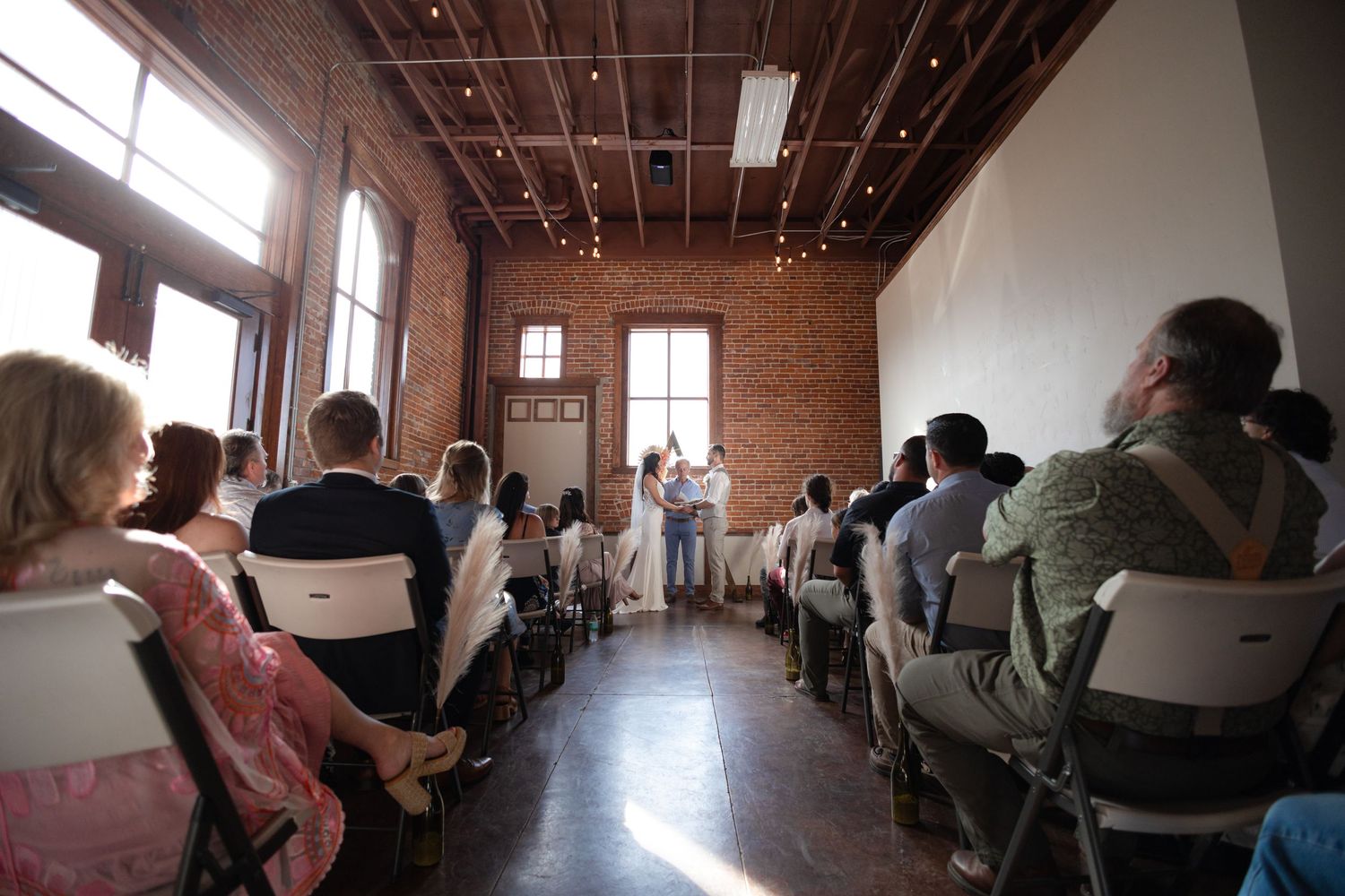 Wedding ceremony guests seated in rows inside a rustic brick venue with natural lighting.