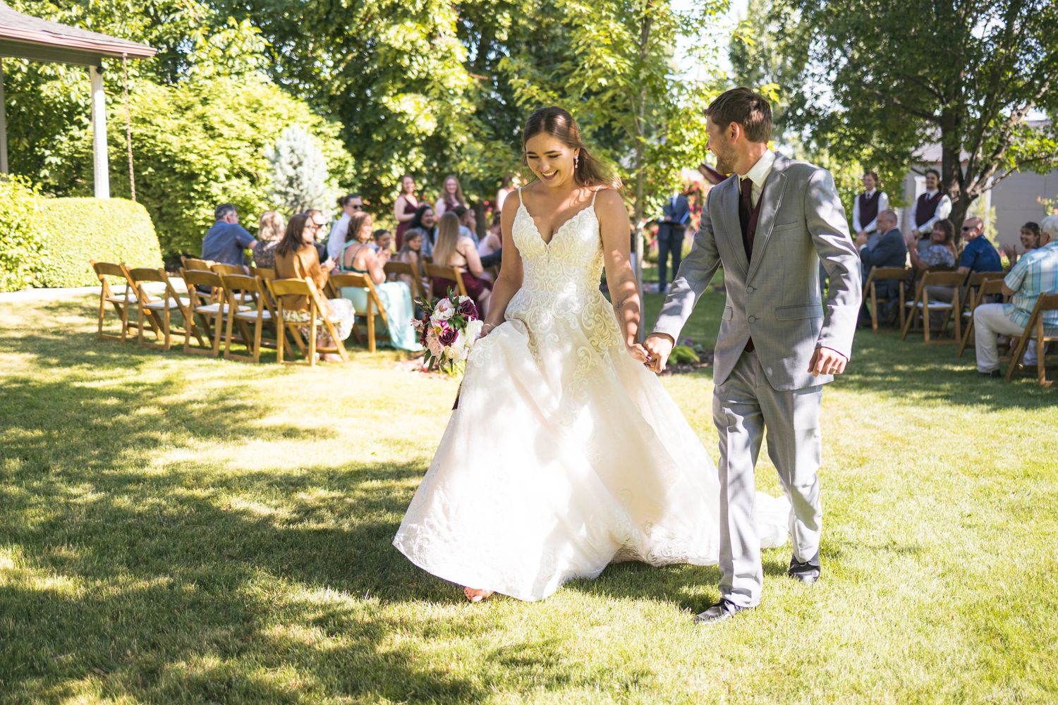 Joyful wedding recessional on a sunny day with guests watching from garden chairs.
