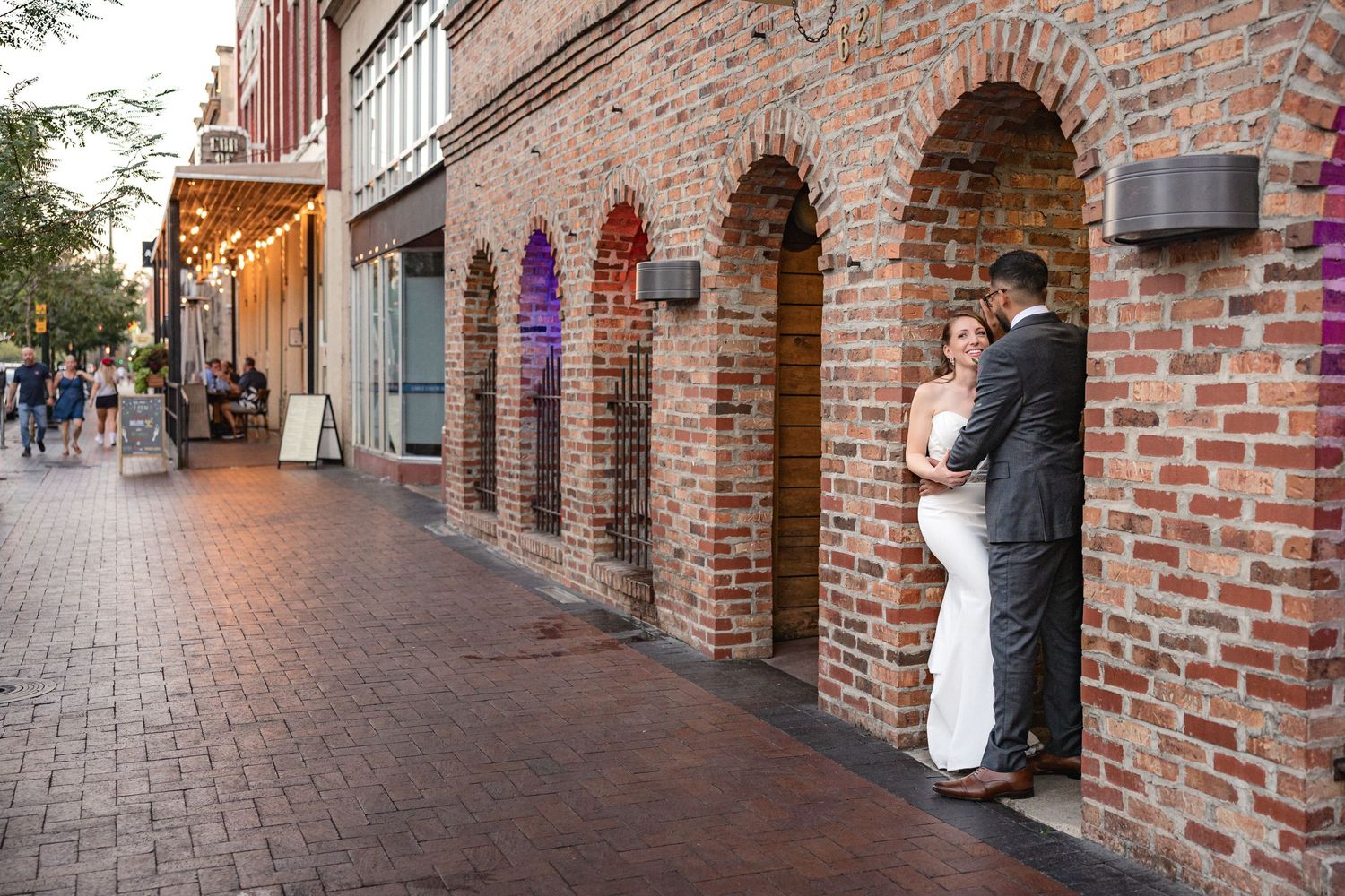 Wedding couple embraces in a brick archway along a historic downtown street.