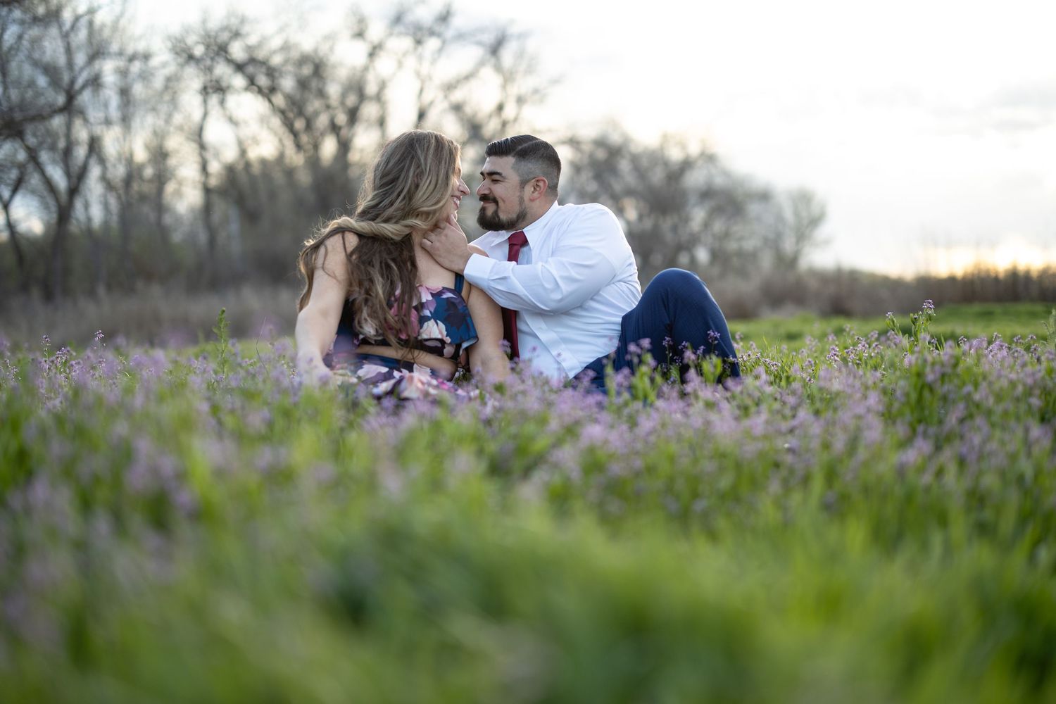 Couple shares tender moment while sitting among purple wildflowers in a meadow.