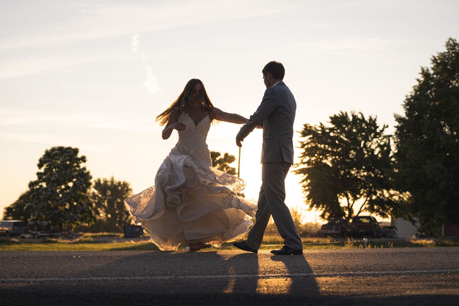 Silhouetted couple dancing in sunset light, with bride's dress flowing dramatically.