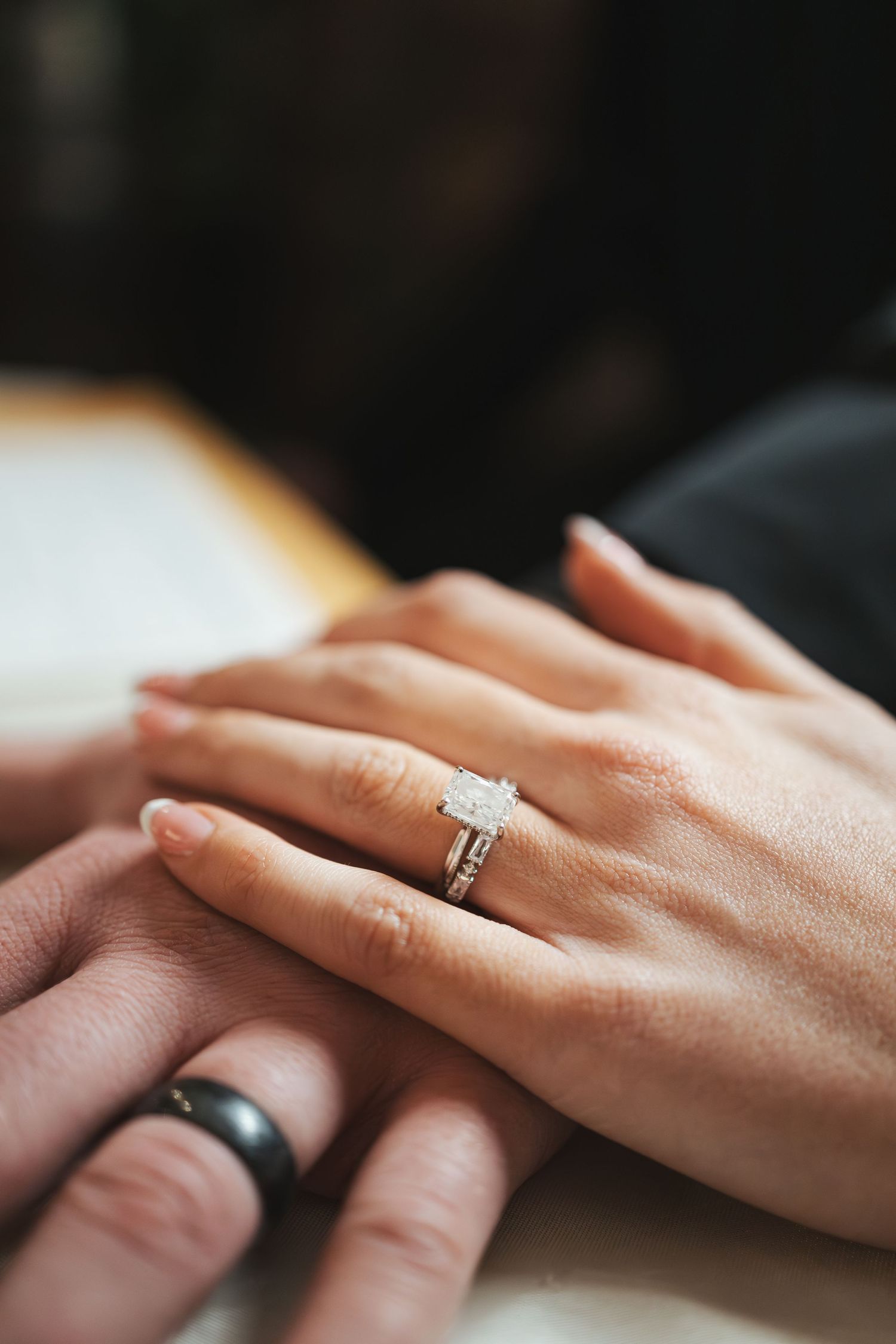Close-up of wedding rings with diamond engagement ring on joined hands.