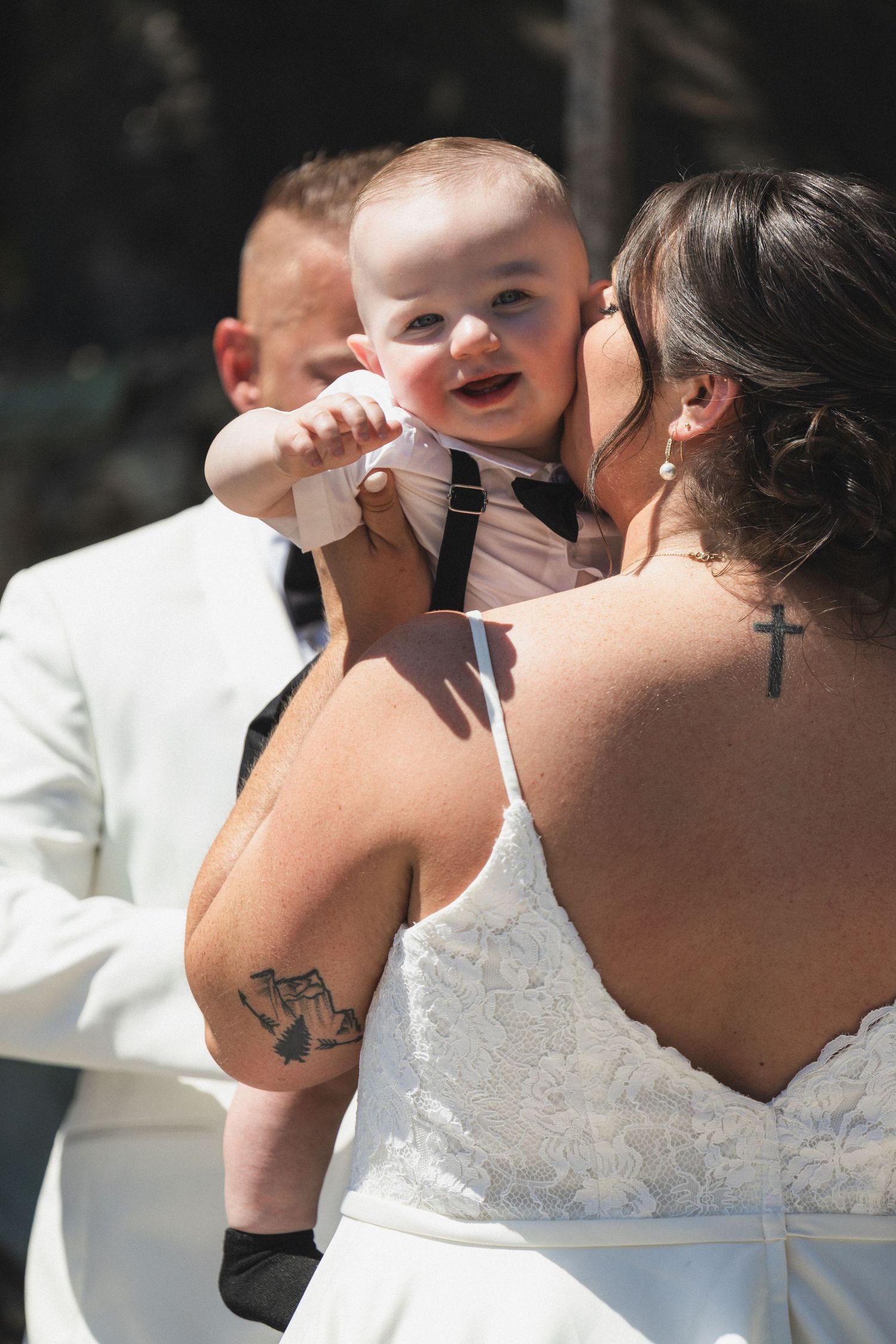 A tender moment between a bride in a white dress holding a baby in formal wear.