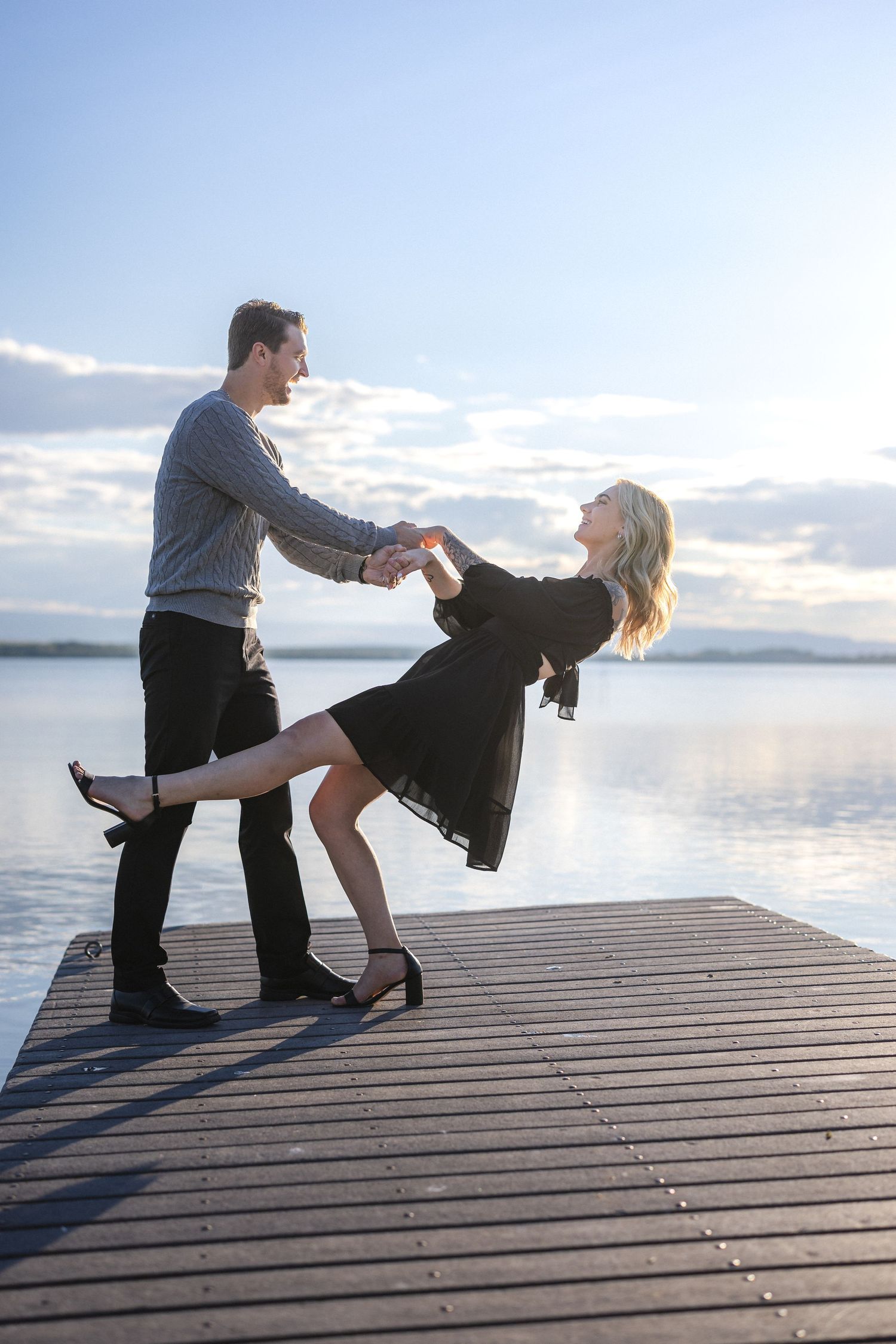 Dancing couple performing romantic dip move on lakeside dock at dusk.