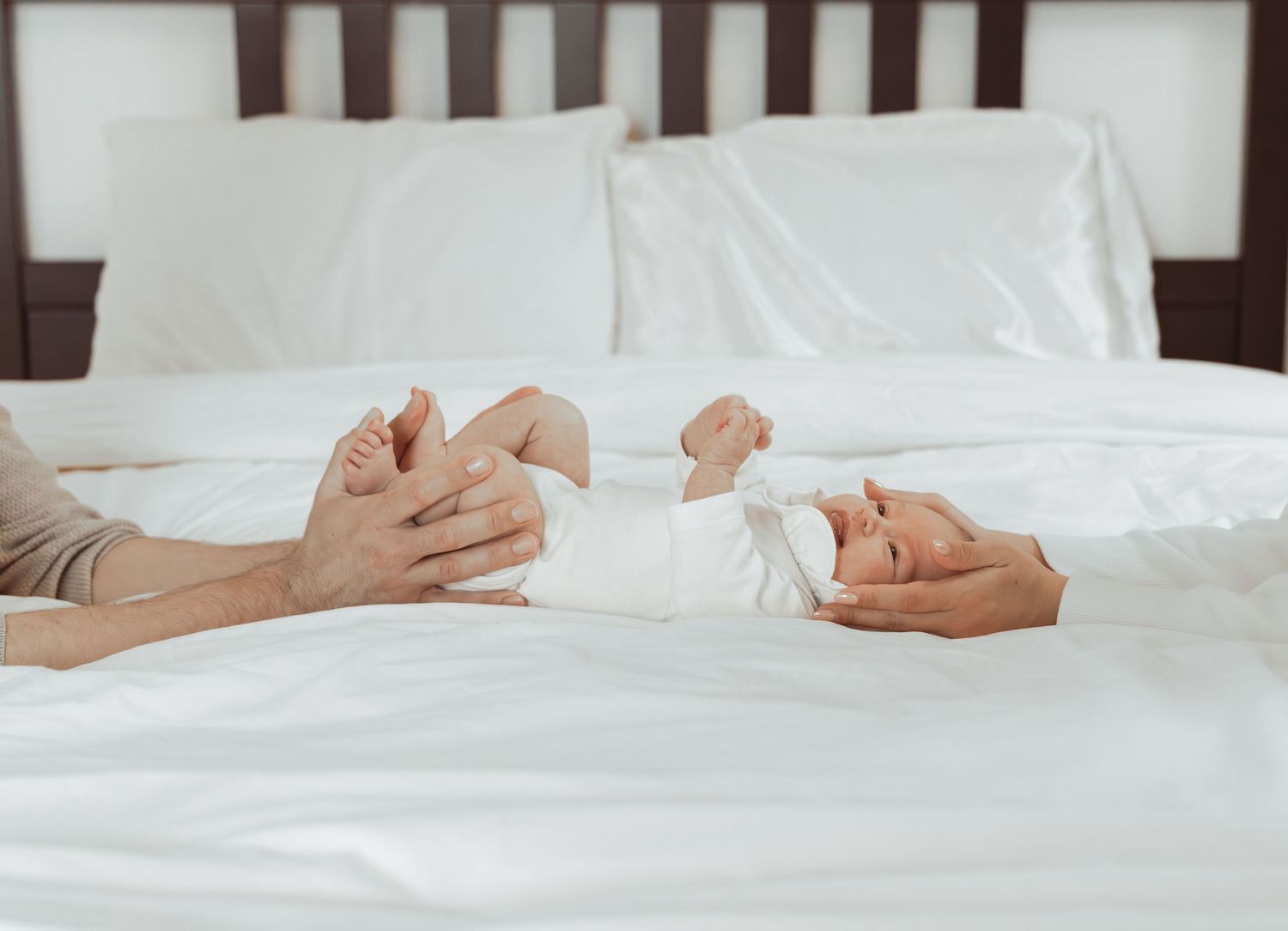 Newborn baby laying on a bed held by parents during an intimate lifestyle newborn photoshoot at home.
