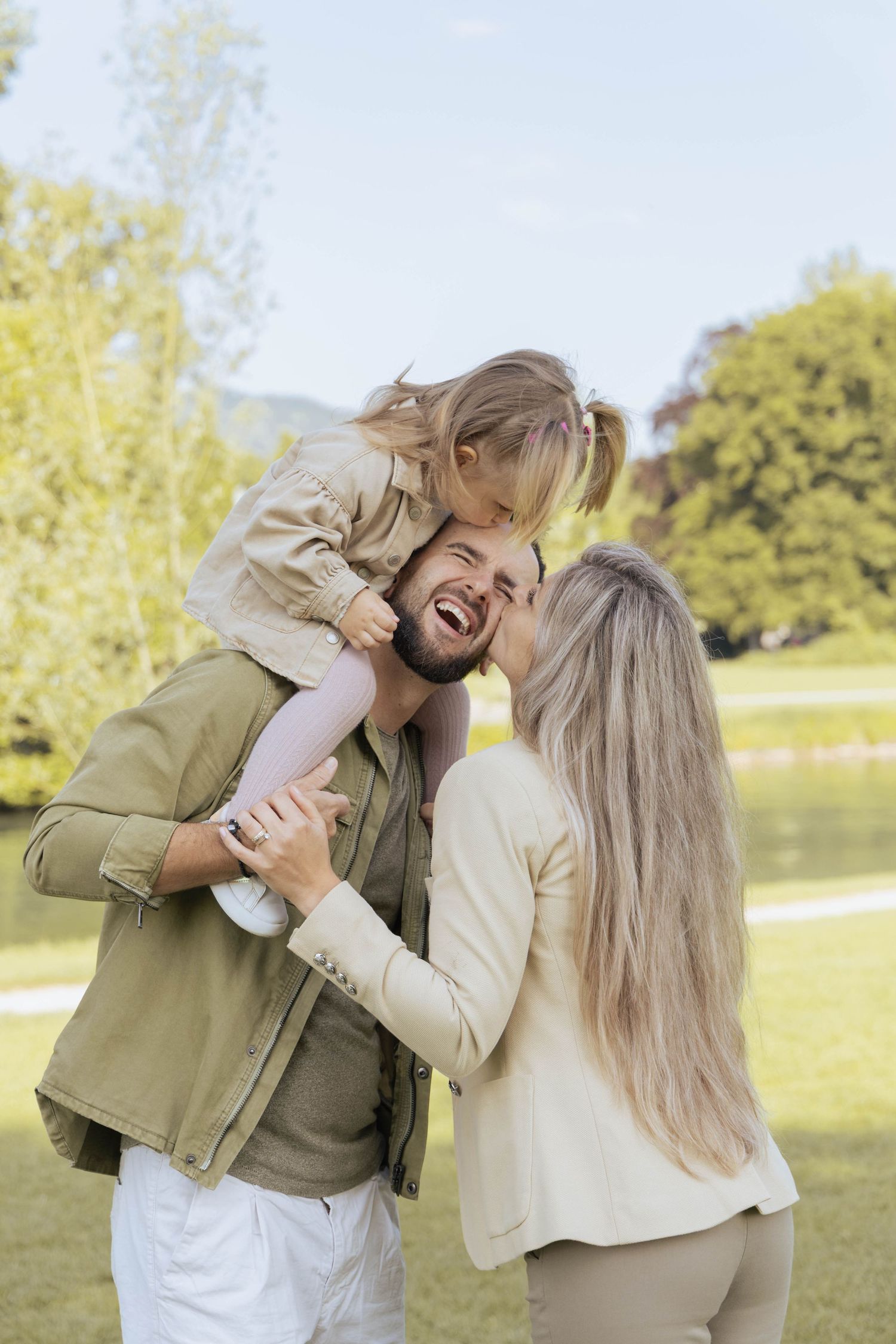 Mother and daughter kissing the father during a joyful family photoshoot in the park.