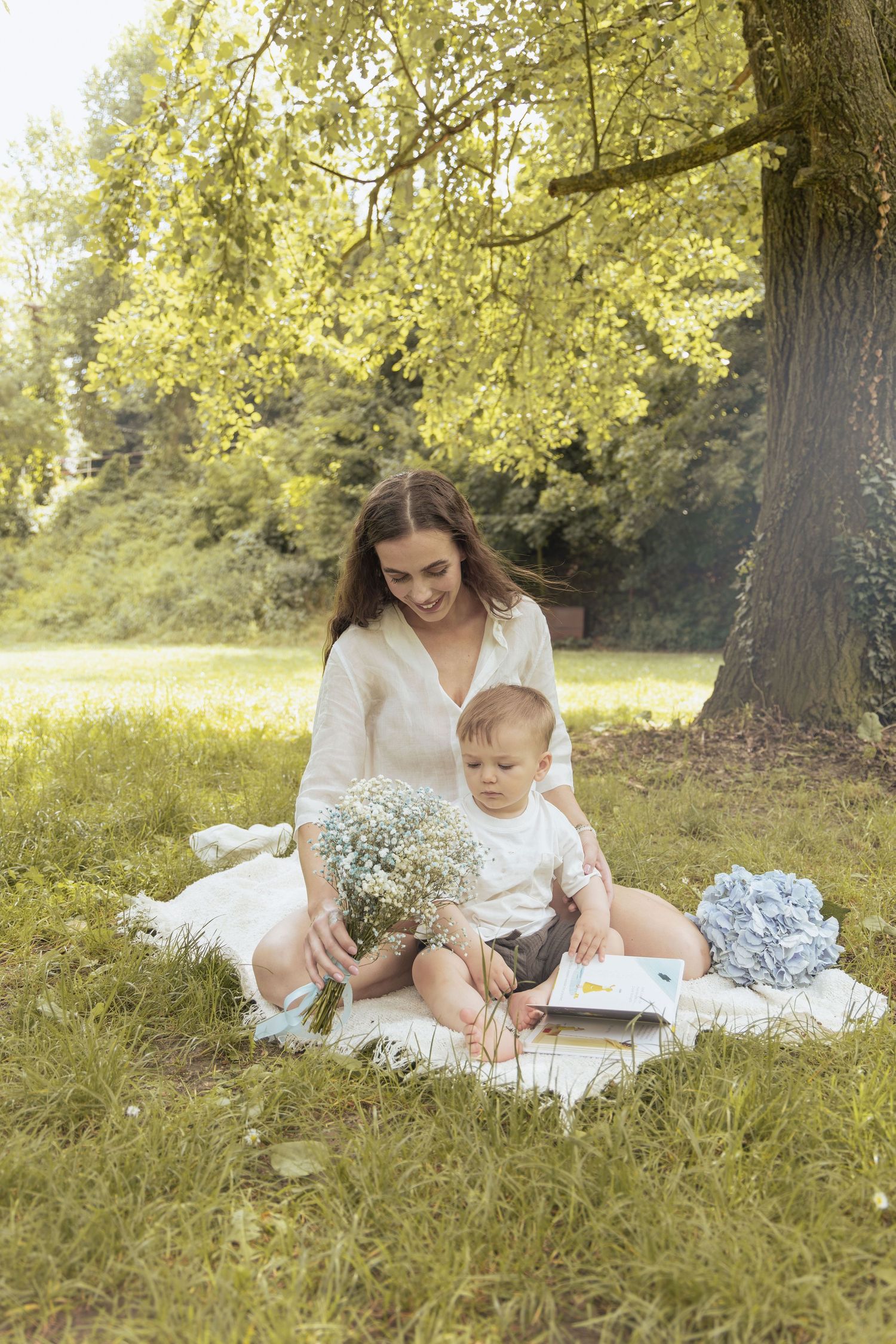 Mother and son sitting on a blanket reading book during a calm family photoshoot outdoors.