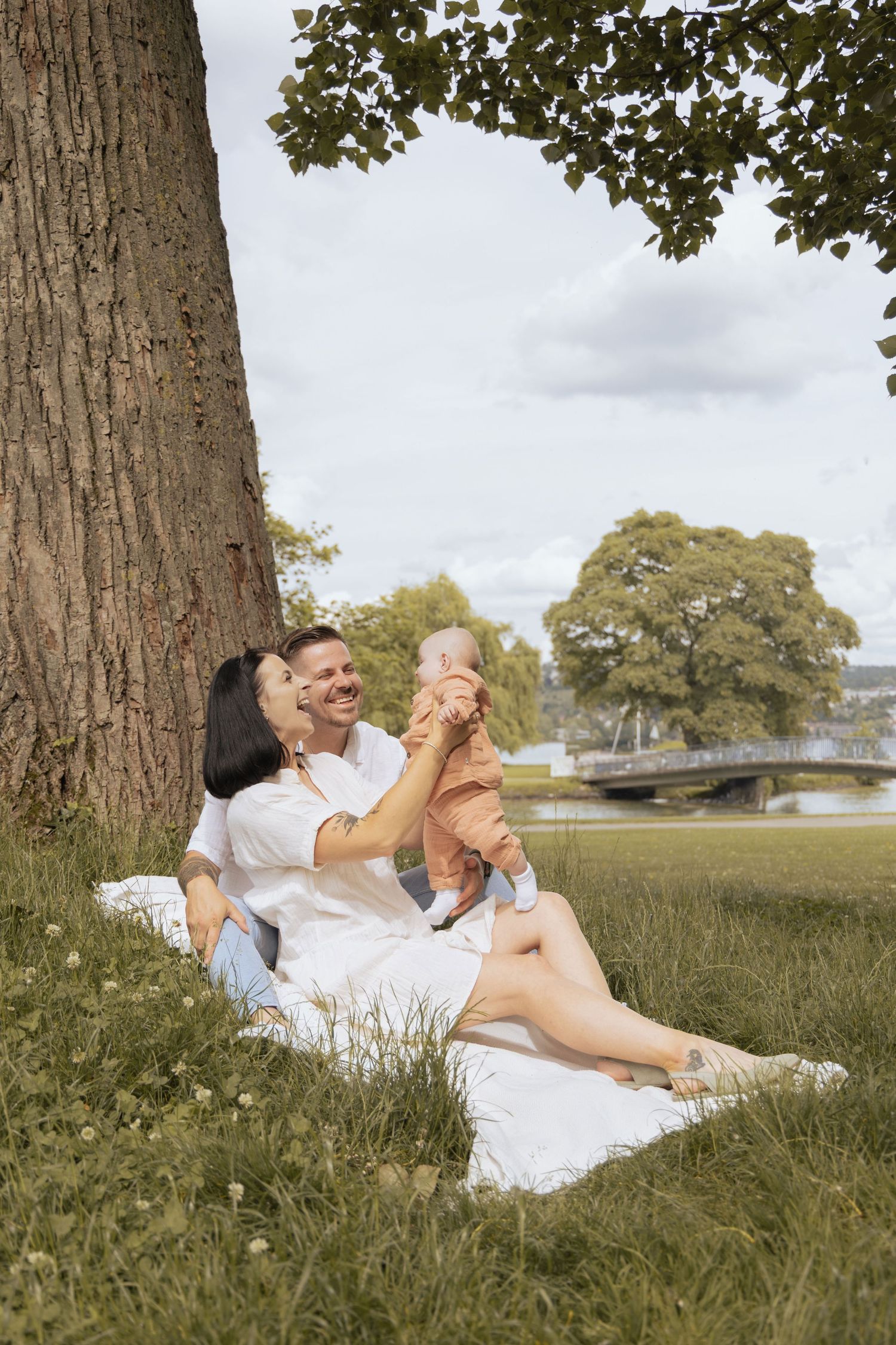 Parents lifting their baby in the air while smiling during a family photoshoot in the park.