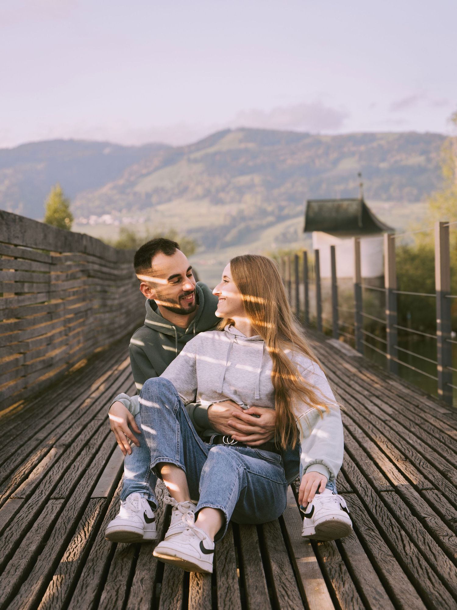 Couple sitting on a bridge with sunlight creating soft shadows during a photoshoot in Switzerland.