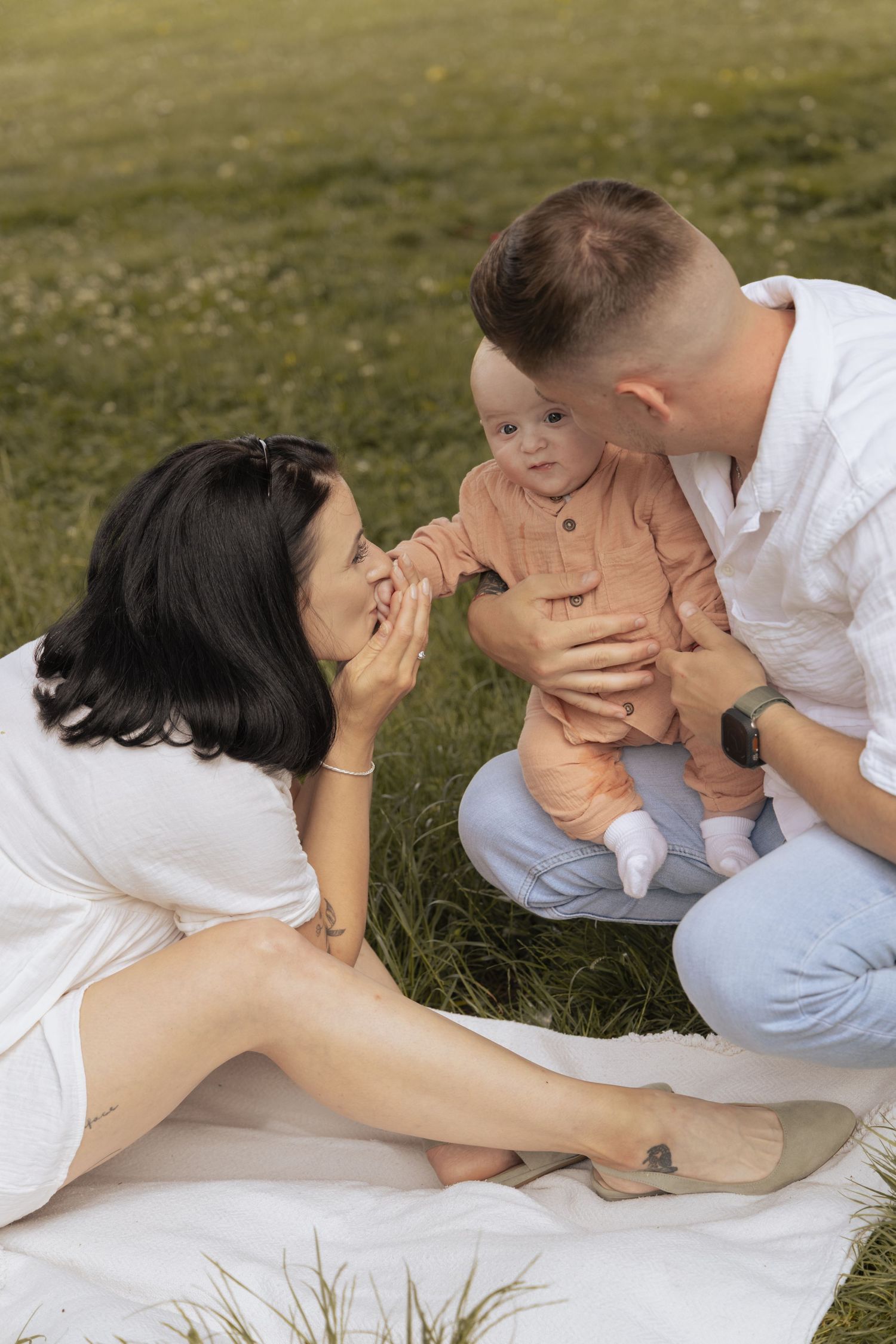 Parents kissing and admiring their baby during a tender family photoshoot outdoors.