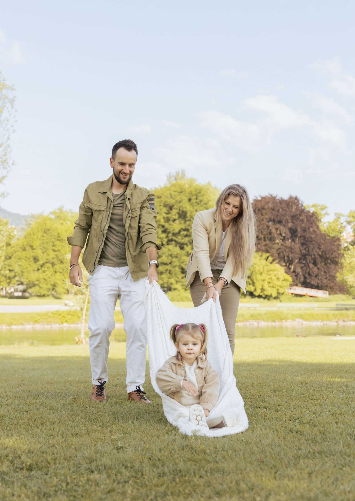 Parents playing with their daughter during a natural family photoshoot in a park.