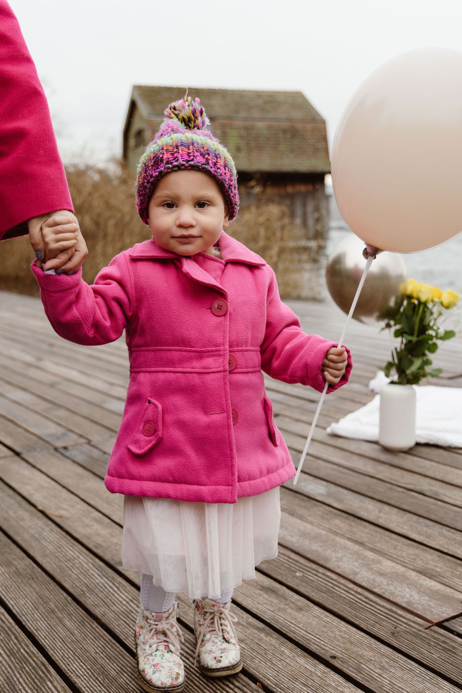 Little girl in a pink coat holding a birthday ballon during a winter photoshoot in Switzerland.