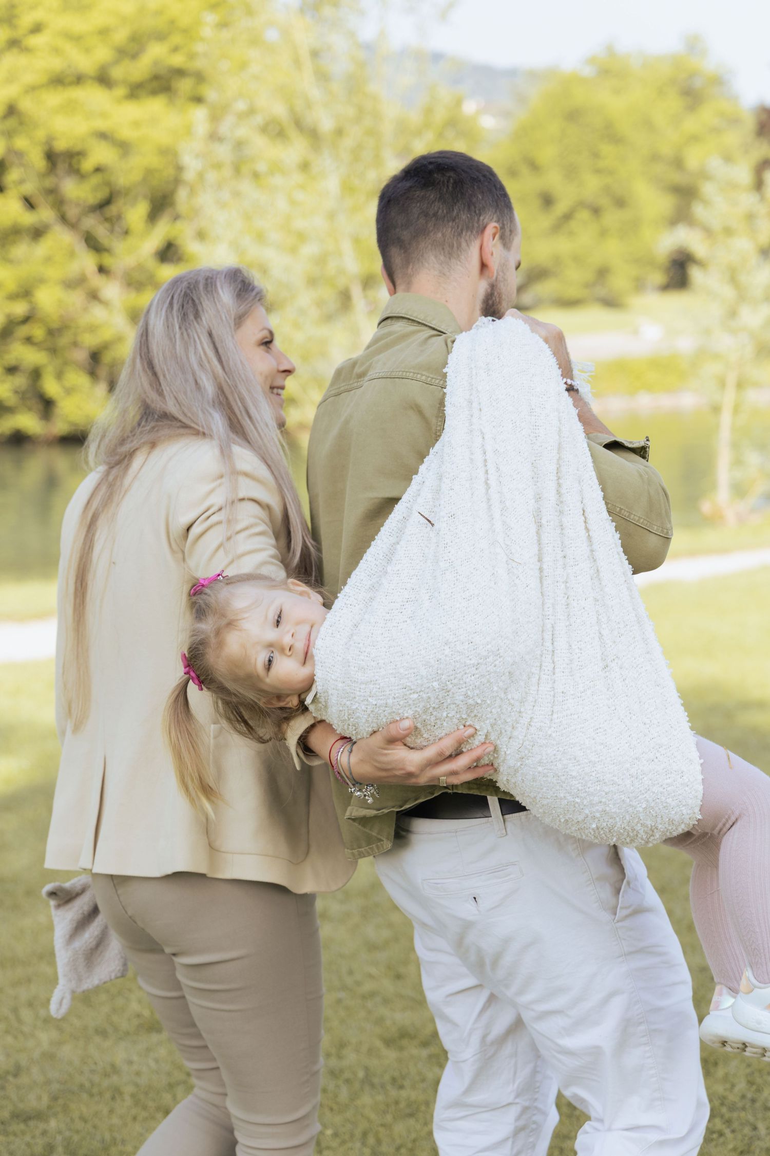 Parents playing with their daughter during a natural family photoshoot in a park.