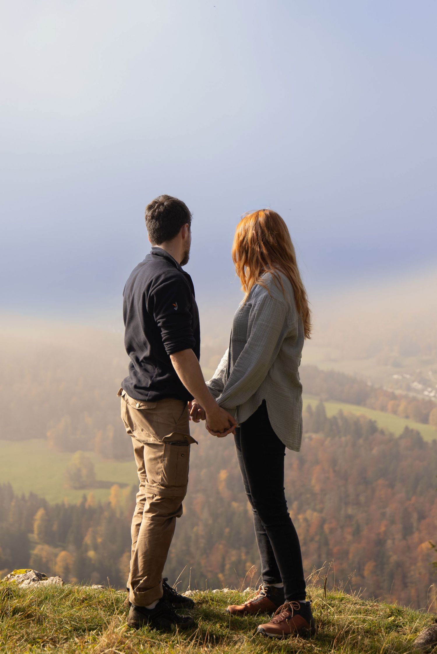Couple standing together and looking at an autumn forest during a photoshoot in Switzerland.